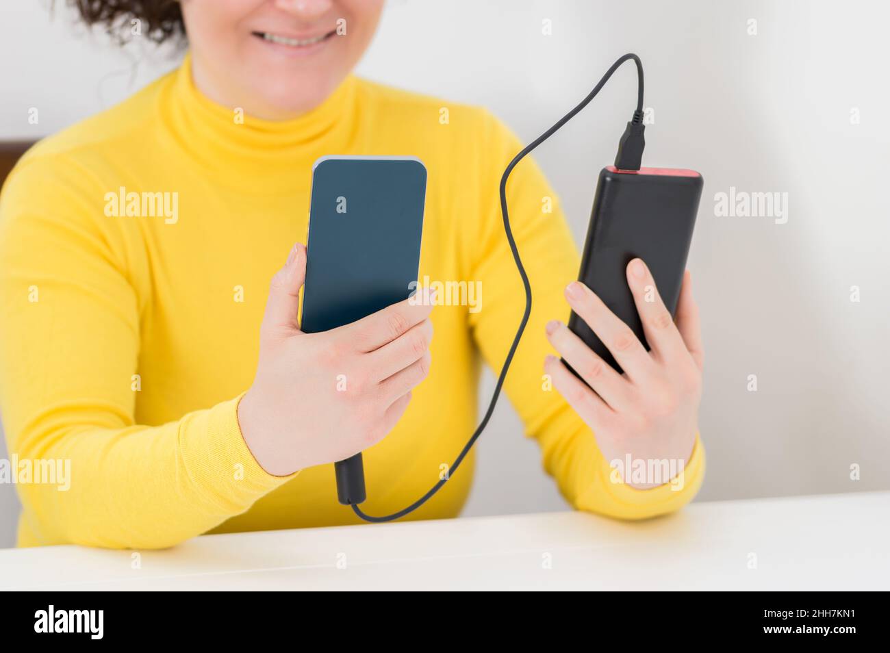 Nahaufnahme einer glücklichen Frau, die ein Smartphone mit einem tragbaren Ladegerät lädt, das zu Hause auf einer Couch sitzt Stockfoto