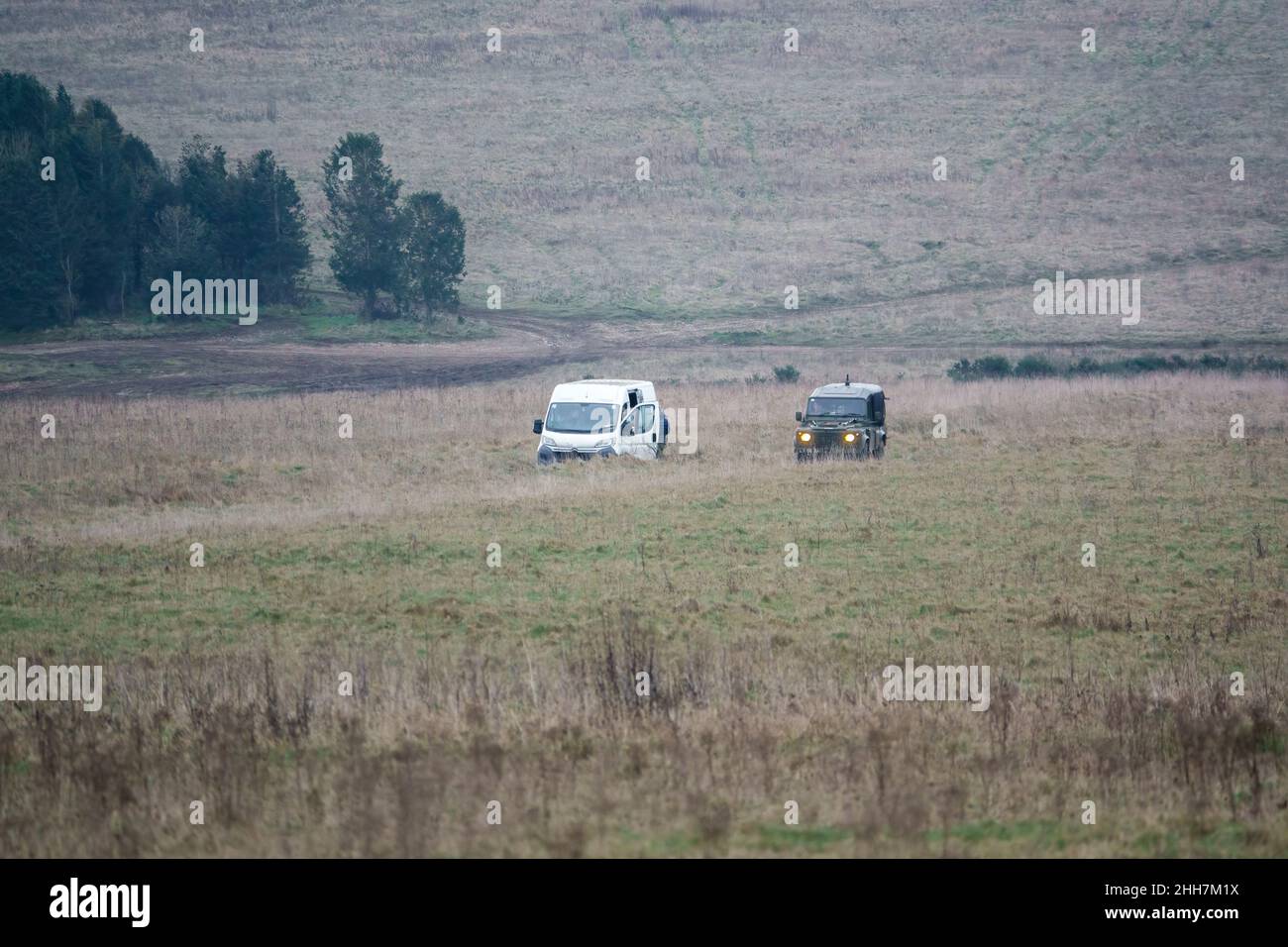 Der mittlere Nutzfahrzeug der britischen Armee, Land Rover Defender Wolf, wird auf einer Schlammspur von einem weißen Fahrzeug heimgesucht Stockfoto