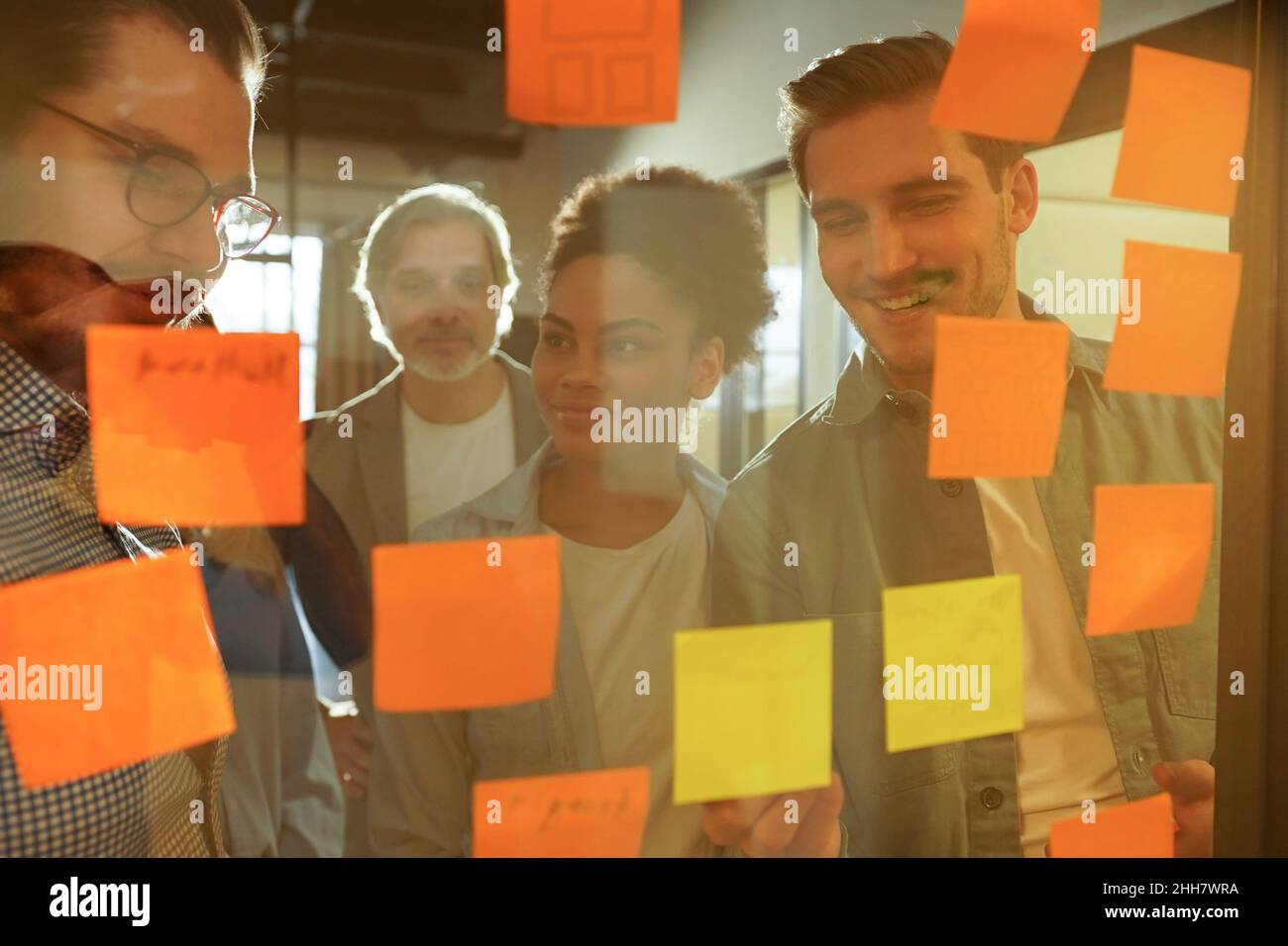 Vielfältige Gruppe von Geschäftsleuten lachend, während er sich in einem Büro gemeinsam Brainstorming mit Haftnotizen auf ein Glas Wand Stockfoto