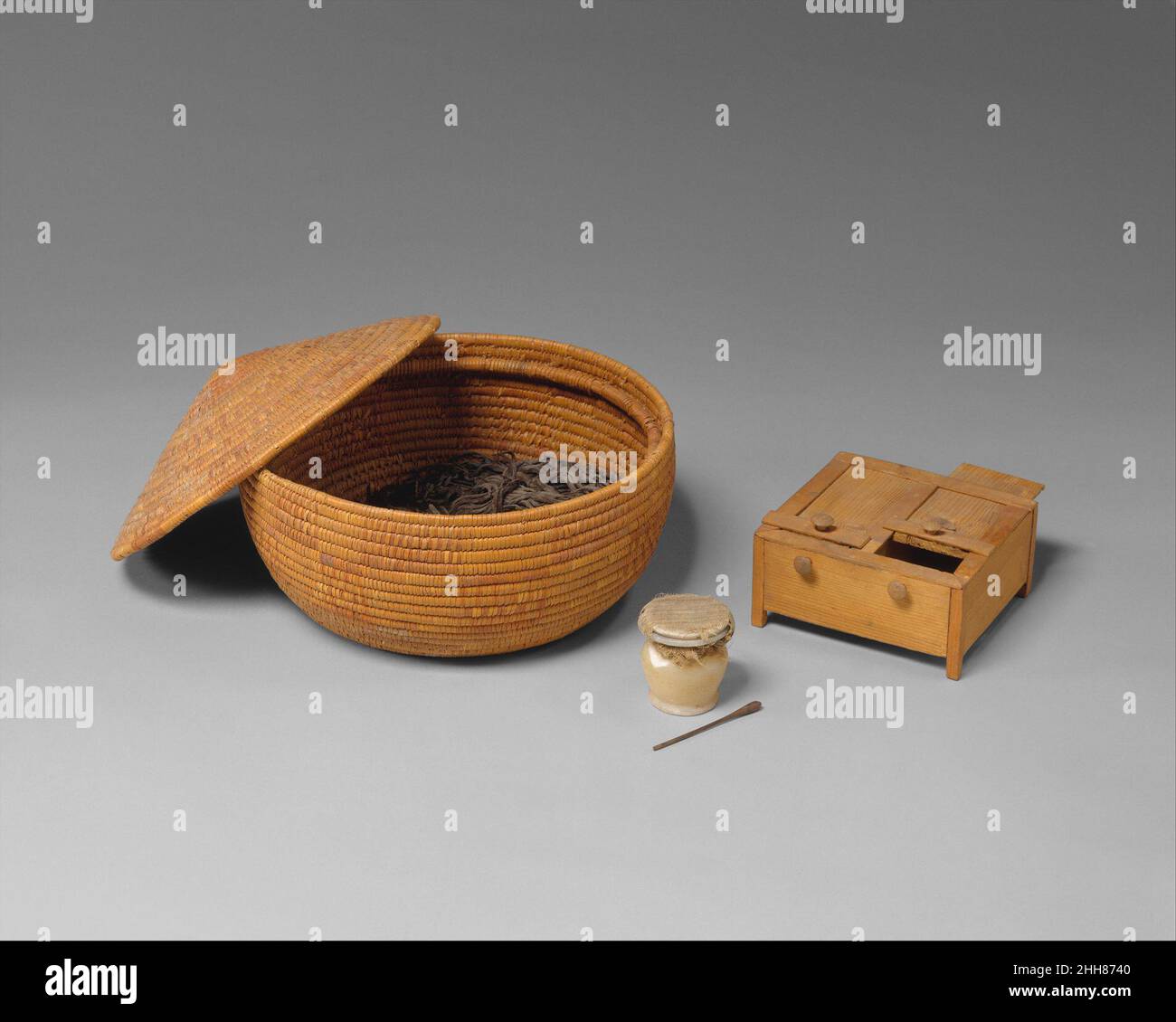 Korb- und Toilettenartikel ca. 1479–1458 v. Chr. Neues Königreich die hier gezeigten Objekte wurden mit der Beerdigung einer namenlosen Frau entdeckt, die etwa zur gleichen Zeit wie Hatnefer lebte. Der Korb enthält eine Masse von feinen Zöpfen aus dunkelbraunem Menschenhaar und drei Bündeln lockerer, welliger Schlösser. Diese Haarsträhnen wurden verwendet, um die eigenen Haare des Besitzers zu vermehren, um die modische Frisur der Zeit zu schaffen. Der Deckel des kleinen Alabasterglases wurde mit einem Stoffreste bedeckt, der mit Leinenschnur gebunden ist, um den Inhalt – das pudrige Augen-Make-up, das als kohl bekannt ist – vor dem Auslaufen zu bewahren. Wenn gefunden ins Stockfoto