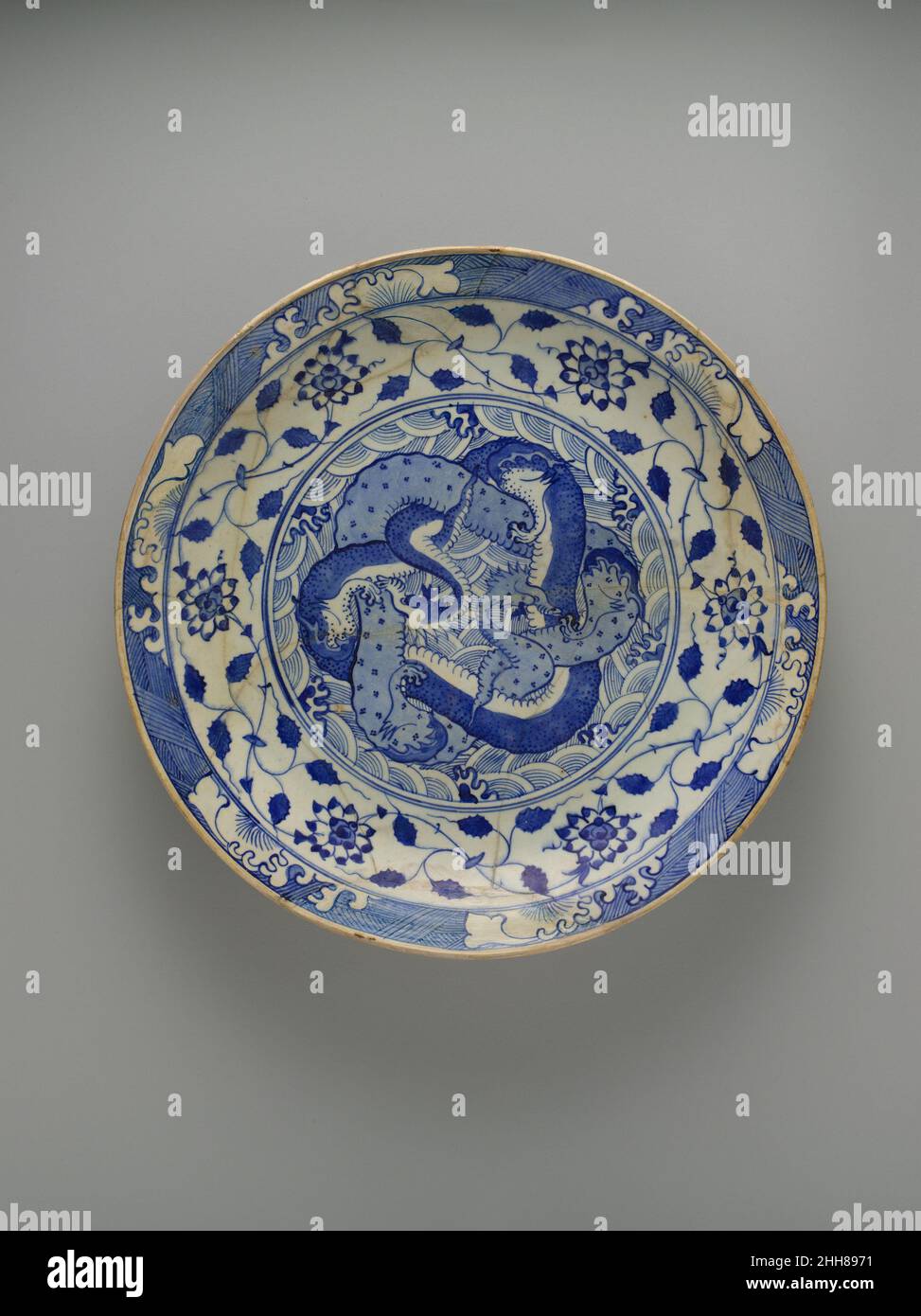 Gericht mit zwei ineinander verflochtenen Drachen Ca. 1640 Obwohl chinesisches blau-weißes Porzellan seit dem 14. Jahrhundert einen starken Einfluss auf die Keramikproduktion des islamischen Nahen Ostens ausgeübt hatte, trat dieses Phänomen im 17. Jahrhundert in eine neue Phase ein, als persische Keramiker auf den Geschmack im Safavid Iran und im Ausland für chinesisches Exportporzellan reagierten, Bekannt als Kraak Ware.die Designs auf diesem großen Teller passen Elemente aus chinesischem blau-weißem Porzellan verschiedener Datteln an. Die Mitte der Schale ist dicht mit zwei verschlungen Drachen geschmückt, einer hellblau und der andere dunkelblau mit einem wh Stockfoto
