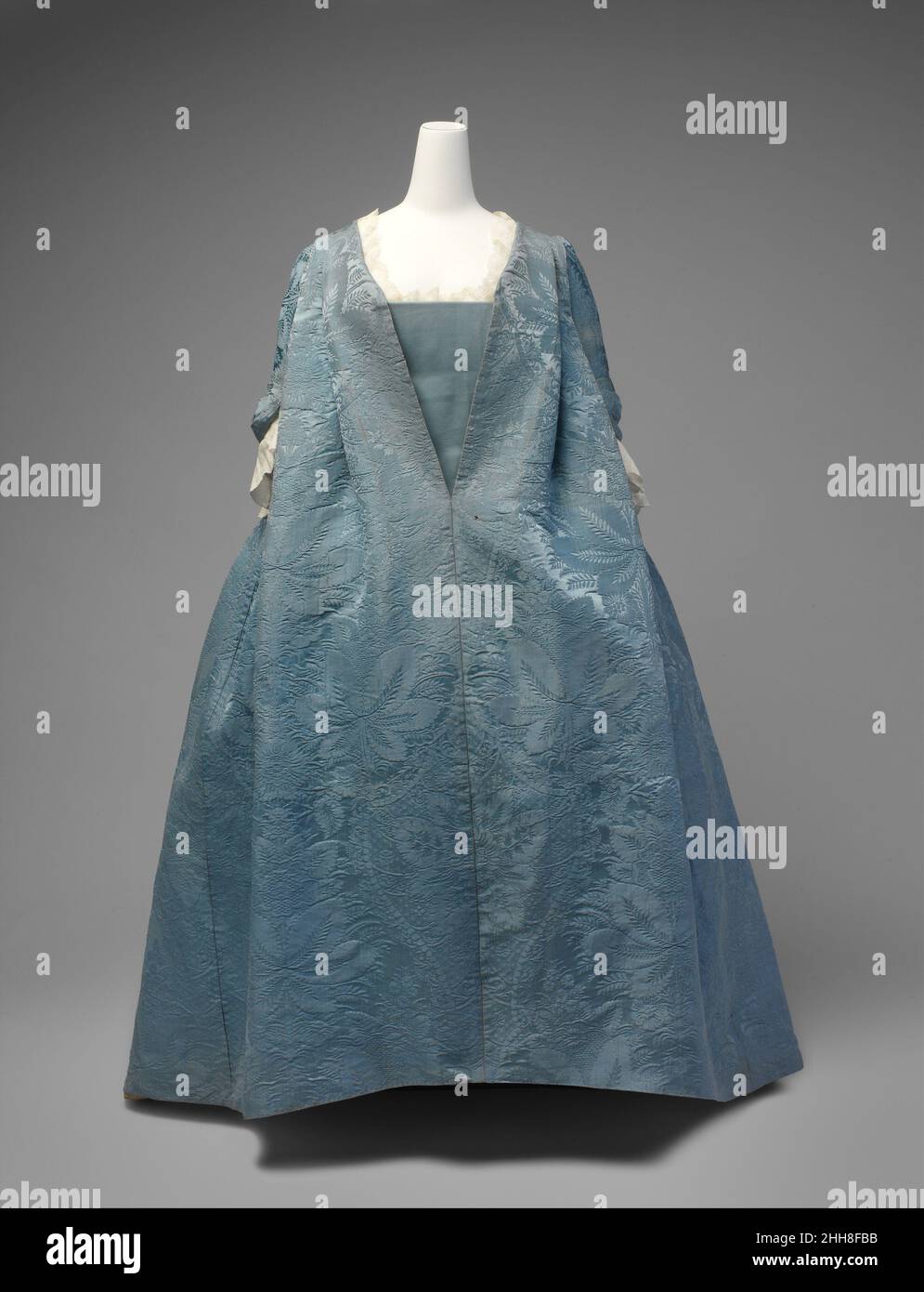 Robe Volante ca. 1730 Französisch Diese Robe volante ist ein äußerst seltenes Beispiel für eine gut dokumentierte Form des Kleides, die den Übergang von der mantua des späten siebzehnten und frühen achtzehnten Jahrhunderts zu der Robe à la française markiert, der Kleiderstil, der im achtzehnten Jahrhundert allgegenwärtig wurde. Die unstrukturierte Silhouette der Robe volante, mit ihren ungebrochenen Stoffweiten, machte sie besonders geeignet für die Darstellung von großformatigen Mustern. Robe Volante. Französisch. Ca. 1730. Seide Stockfoto