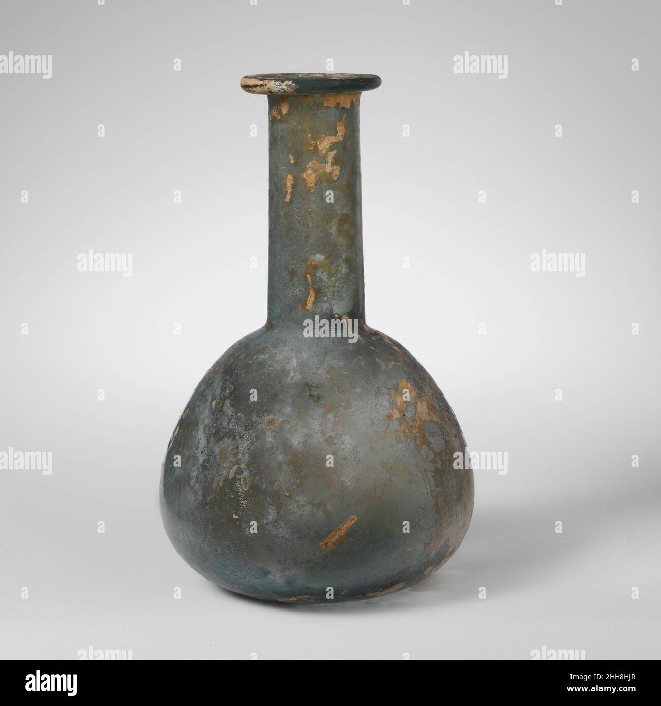 Parfümflasche aus Glas 1st–2nd Jahrhundert n. Chr. römisch Durchscheinendes blaugrün.unebener Rand, der nach außen, nach innen und oben ausgeklappt und flach gedrückt wurde, was zu Engstellen im Mund führte; zylindrischer Hals, der sich leicht nach unten ausdehnt, mit Werkzeugmarkierungen um seine Basis; Knollenkörper; gebohrter Boden, in der Mitte flach. Intakt; einige größere und Nadelblasen; Lochfraß, Abstumpfen und Schillern; Flecken emailliger Verwitterung. Parfümflasche aus Glas 239610 Stockfoto