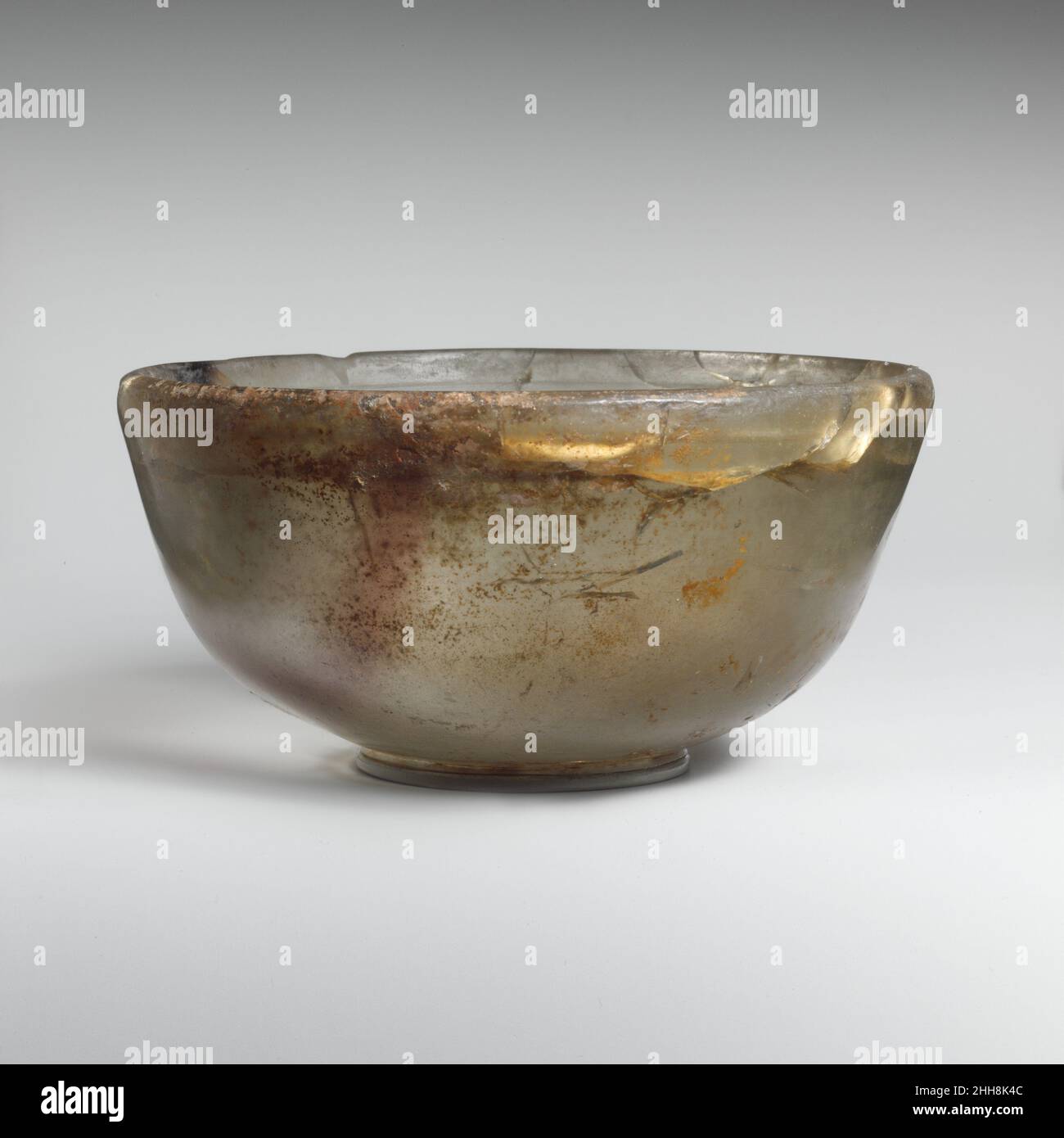 Glasschale Mitte 2nd–Anfang 1st Jahrhundert v. Chr. Griechisch, östliches Mittelmeer farblos mit durchscheinendem violettem Streifen.unebener, eckiger und leicht umgekehrter Rand; halbkugelliger Körper mit gerader Seite, schräg nach unten zulaufend und dann eingebogen; konvexer Boden.im Inneren zwei horizontale Rillen in einem Band unter dem Rand geschnitten; Außen ein Band aus zwei leicht abrassierten Rillen um den Boden mit kleinem Kreis in der Mitte.intakt, aber viele interne Dehnungsrisse um die Seite unter dem Rand und im Boden; einige Nadelstiche Blasen; isolierte Flecken von tiefem Lochfraß und bräunlich schillernder Verwitterung.drehschleifmaschine ma Stockfoto