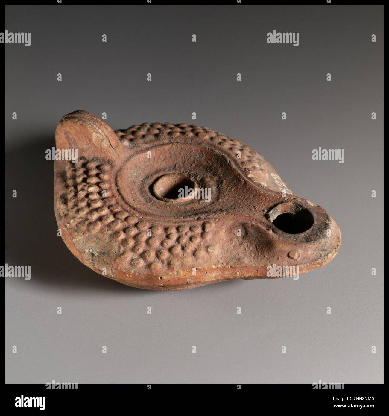 Terrakotta-Öllampe 3rd Jahrhundert A.D. Roman Vessberg Typ 18. Formgefertigte, mit undurchbohrtem Griff. Discus: Undekorierter Kreis, mit zentralem Einfüllloch und umrandet von einer erhöhten Linie und Nut, die sich nach vorne ausdehnen und das Dochtloch umschließen. Konvex-geschwungene Schulter: Muster von erhöhten Kügelchen. Erhöhter Basisring, flankiert von runden Nuten, und kleiner, eingesteckter Sockel, möglicherweise mit einem Fußabdruck-Stempel beeindruckt. V-förmiges Muster aus Linien und Nuten zwischen Sockel und Griffrückseite; zwei Bänder aus zwei parallelen Nuten, die die Unterseite der Düse flankieren, und eine Reihe von drei eingeprägten Punkten auf der Rückseite der Düse.intakt Stockfoto
