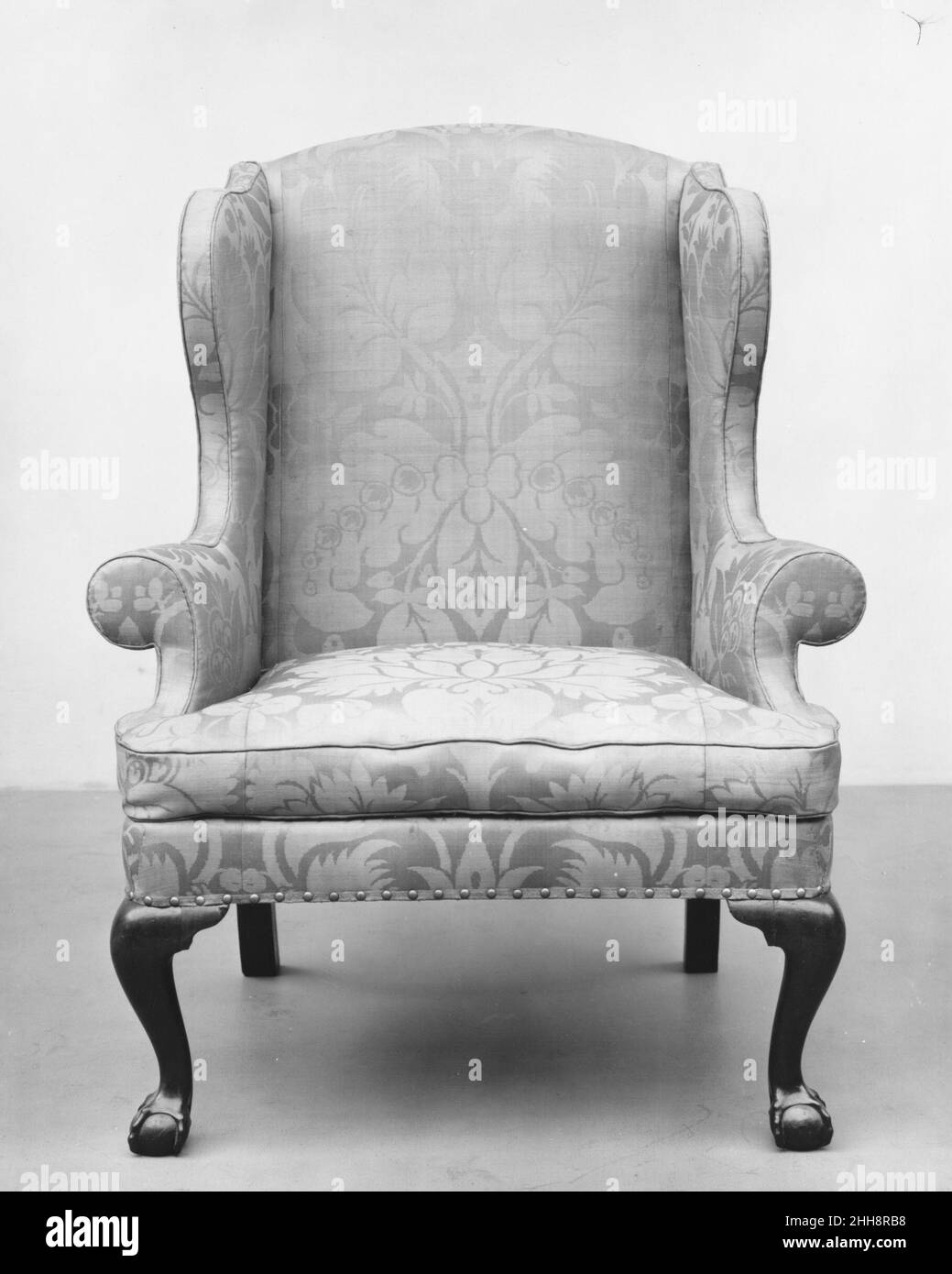 Sessel 1755–90 Amerikaner ein Sessel war das Produkt zweier verschiedener Handwerker. Der Stuhlhersteller baute den Holzarmatur, der die Grundrisse des Stuhls bestimmte, während der Polsterer seine endgültige Form feststellte. Obwohl die C-Scroll-Arme typisch für die Arbeit in Philadelphia sind, wurde dieser Stuhl in New York City hergestellt. Die Sekundärhölzer sind in New Yorker Möbeln üblich, ebenso die quadratischen Hinterbeine und die Art, wie die Sitzschienen mit den Vorderbeinen verbunden werden. Außerdem sind die Klauen-und-Ball-Füße, die sich durch einen gequetschten Ball mit schmalen, nach unten abfallenden Talonen auszeichnen, deutlich Ne Stockfoto
