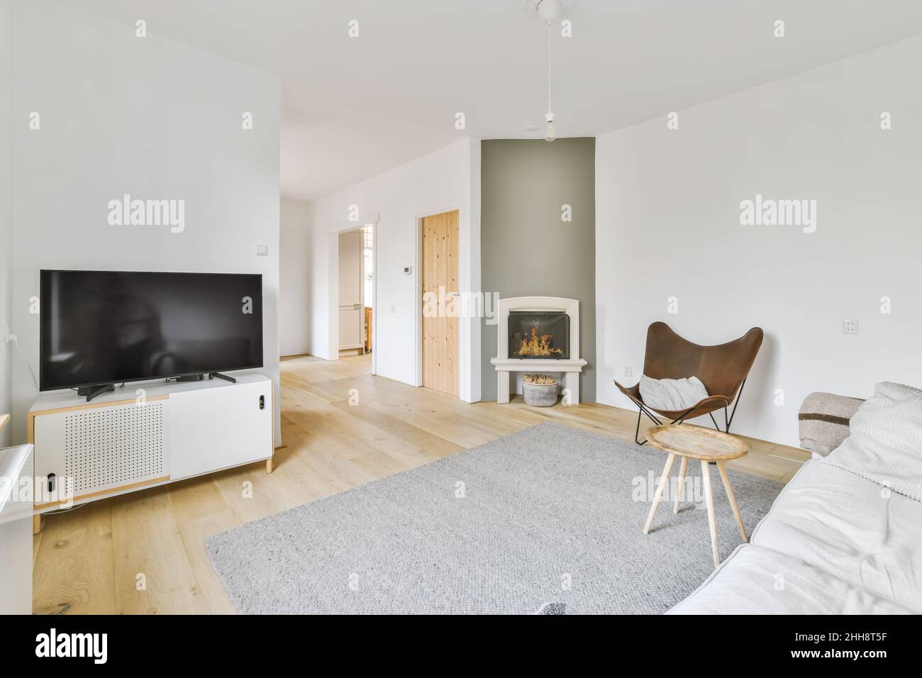 Echtes Foto eines gemütlichen Wohnzimmers mit Kamin, Fernseher, einem runden Tisch auf grauem Teppich, einem stilvollen Stuhl und einem weißen Sofa neben dem Flur Stockfoto