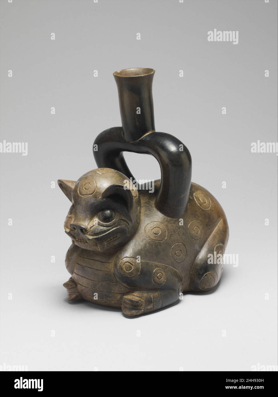 Feline Bottle 600–400 v. Chr. Tembladera eine ungewöhnliche Gefäßform, bekannt als die Steigbügelflasche mit Auslauf, erschien während der Formationsperiode (1800–200 v. Chr.) mit der Kultur der Cupisnique an der Nordküste Perus. Der Name „Steigbügel-Auslauf“ bezieht sich auf eine Flasche mit einem Auslauf, der der Fußstütze eines Reitsattels ähnelt. Dieses Stück soll an der archäologischen Stätte von Tembladera (1200–800 v. Chr.) im Jequetepeque-Tal gefunden worden sein, wo es wahrscheinlich eines von mehreren repräsentativen Objekten war, die in einem Grab aufgestellt wurden. Sein trapezförmiger Griff mit langem, abfackeln Hals ist typisch für die Keramikgefäße aus dieser reg Stockfoto