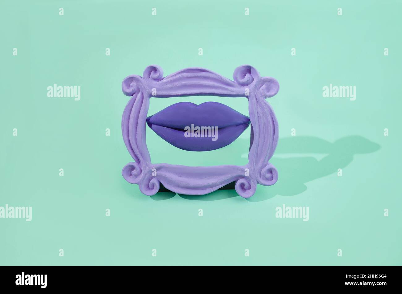 Große Lippen mit violettem Lippenstift in einem Retro-lila Rahmen auf pastellgrünem Hintergrund. Surreales kreatives Konzept für Valentines Banner. Artistick Design für Stockfoto