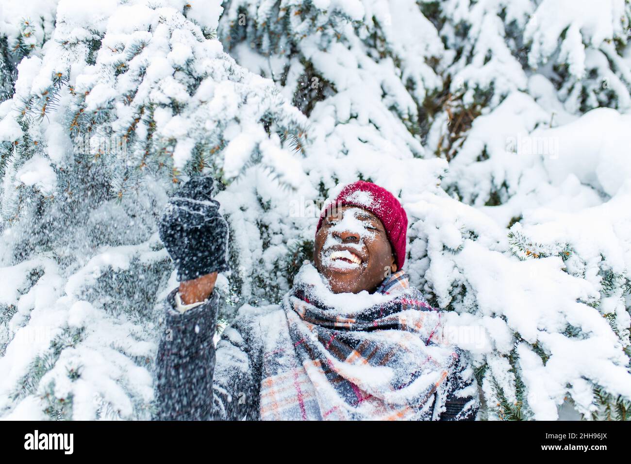 afroamerikanischer Handsom-Mann in rotem Hut und stilvollem karierten Mantel Blick auf die Kamera mit toothy schneeweißen Lächeln im Freien im Park Stockfoto