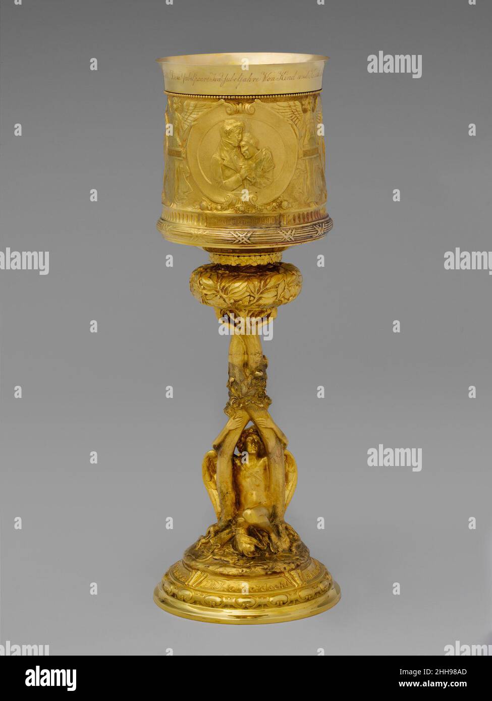 Standing Cup ca. 1900 Entworfen von Karl Theodore Bitter American, Born Austria dieser Kelch verkörpert Beaux-Arts-Empfindlichkeiten, insbesondere in seinem klassischen Vokabular und seinem akribisch geschnitzten und repussé Ornament. Es wurde anlässlich des goldenen Hochzeitstages von Marcus und Bertha Goldman, den Großeltern des Spenders, angefertigt und die Szenen in den Medaillons dokumentieren das Eheleben des Paares. Eros, umarmt die Stämme von zwei miteinander verflochtenen Bäumen, sitzt auf der Basis als Symbol für die anhaltende Liebe des Paares.. Standing Cup. Amerikanisch. Ca. 1900. Gold. Hergestellt in Concord, New Hampshire, USA Stockfoto