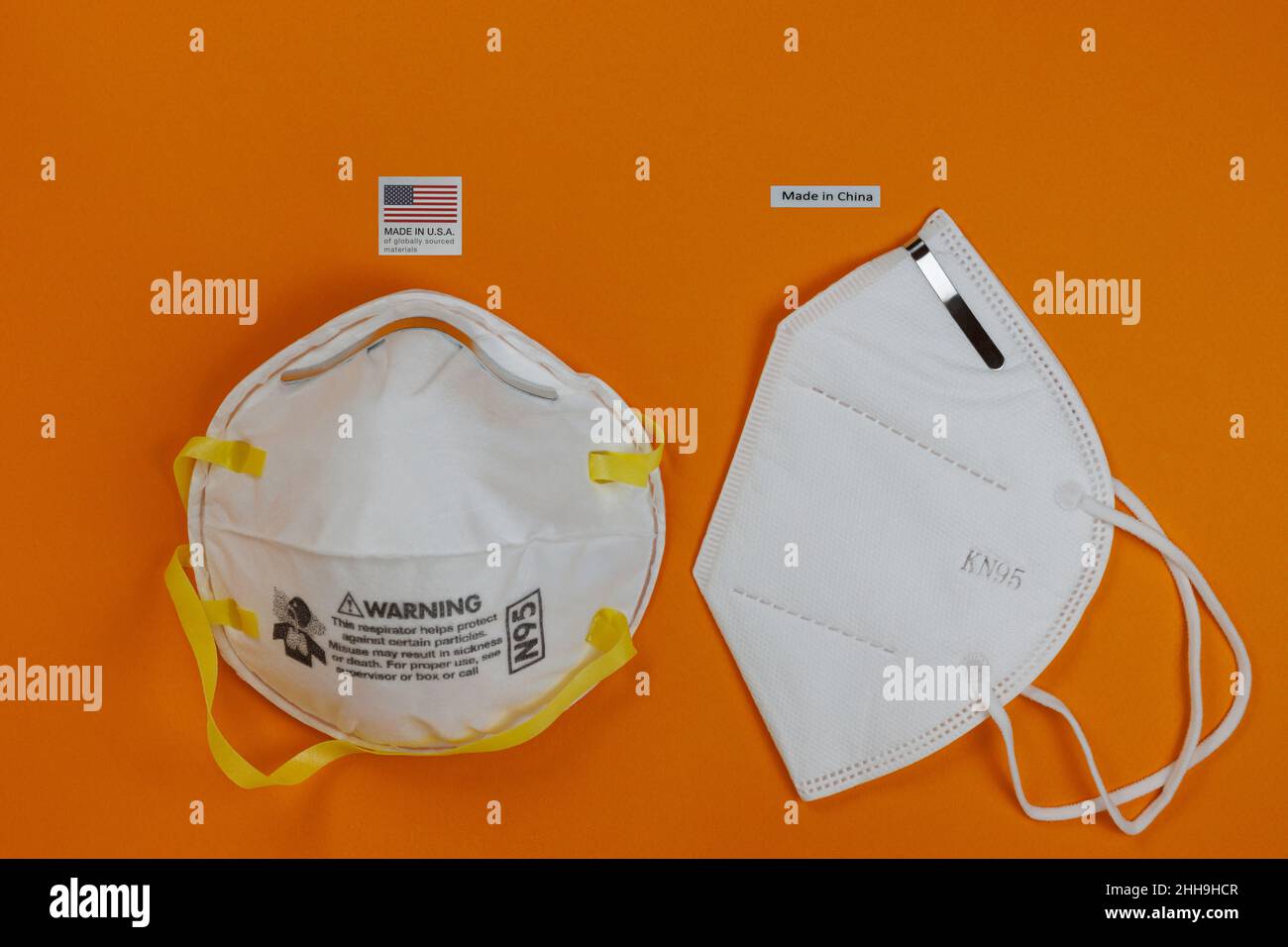 N95 Atemschutzmaske, hergestellt in den USA, neben einer KN95 Gesichtsmaske, hergestellt in China, mit Etiketten oben, auf orangefarbenem Hintergrund Stockfoto