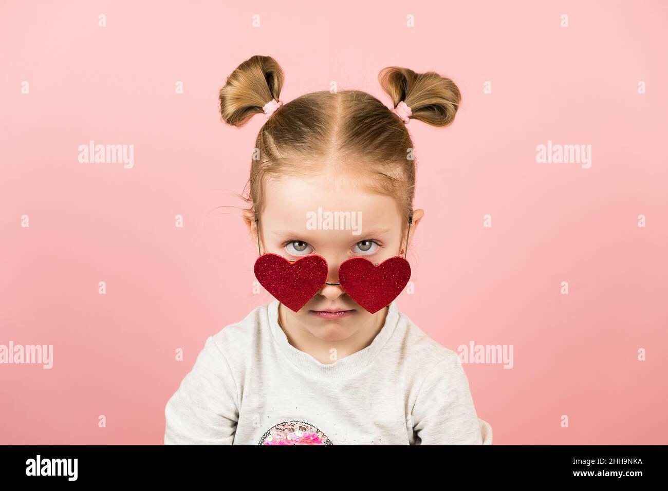 Lustige böse kleine blonde Mädchen in roten herzförmigen Sonnenbrille auf rosa Hintergrund. Valentinstag oder Muttertag Konzept Stockfoto