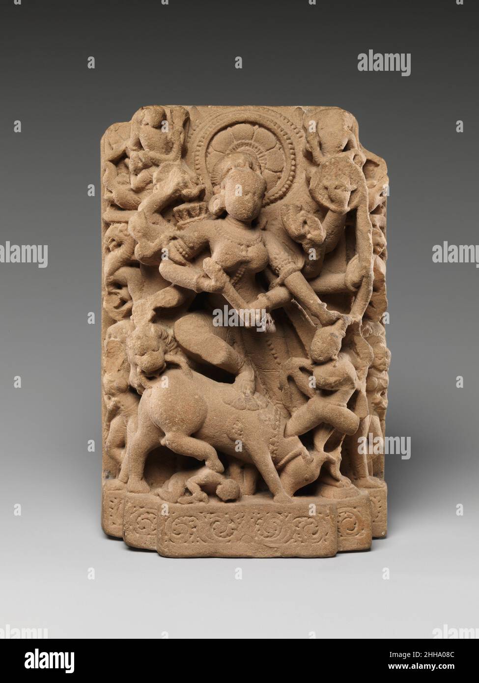 Die Göttin Durga, die den Büffeldämon erschlagen hat (Mahisasura Mardini) 10th. Jahrhundert Indien (Rajasthan) die mehrarmige Durga trampelt den erschlagenen Büffel mit ihrem erhobenen Bein und stürzt ihren Dreizack in die menschliche Form des Dämons Mahisha, der aus dem Hals des Tieres hervortritt. Ihr Fahrzeug, der Löwe, schließt sich dem Kampf an und zermalmt den Büffel von hinten. In dieser feierlichen Ikone, die eine Außennische in einem Hindu-Tempel besetzen soll, wird Durga von Girlande-tragenden himmlischen Dienern (gandharvas) geehrt. Die Göttin Durga, die den Büffeldämon erschlugt (Mahisasura Mardini). Indien (Rajasthan). 10th Centu Stockfoto