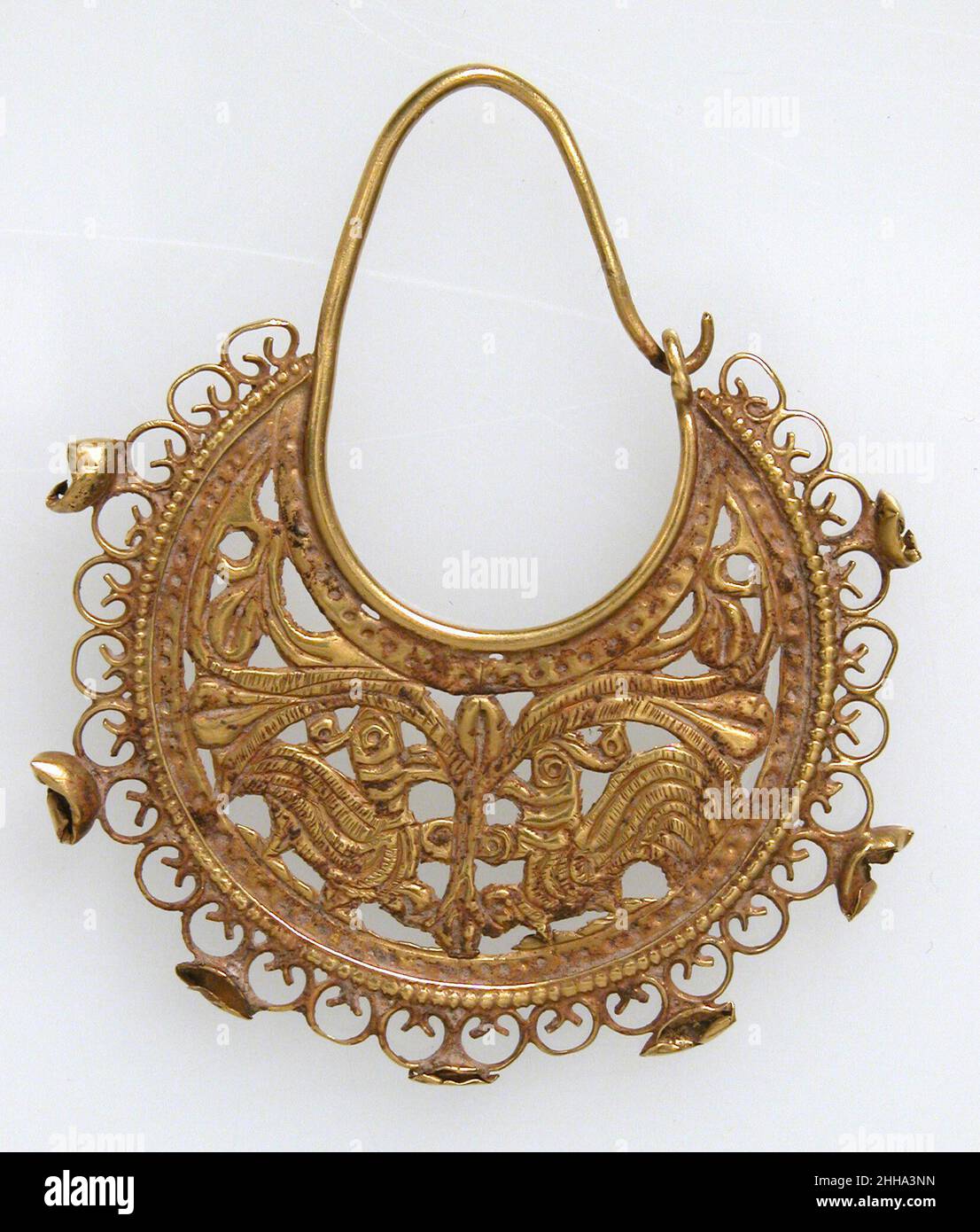 Goldener halbmondförmiger Ohrring mit pfauen Ende des 6th.–7th. Jahrhunderts byzantinischer Opus interrasile war eine Technik, die von Goldschmieden zur Herstellung von elegantem Schmuck von den Jahren 200s bis 600s verwendet wurde. Die Entwürfe wurden auf Goldplatten zurückverfolgt; der Hintergrund wurde mit Löchern in verschiedenen Größen gestanzt, um das Muster hervorzuheben; und feine Details wurden dann an der Oberfläche bearbeitet. Die Muster, die durch Durchstechen des Metallgrundes gebildet wurden, ermutigten das Spiel von Licht und Schatten über die Oberfläche eines Objekts. Goldener halbmondförmiger Ohrring mit pfauen 467645 Stockfoto