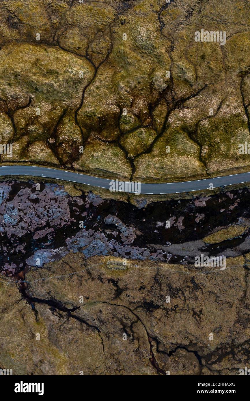 Eine Luftaufnahme zeigt eine Straße, die durch atemberaubende texturierte Landschaften in khaki-Grün, Braun und Schwarz führt, so ungewöhnlich, dass sie fast nicht real aussehen. Stockfoto