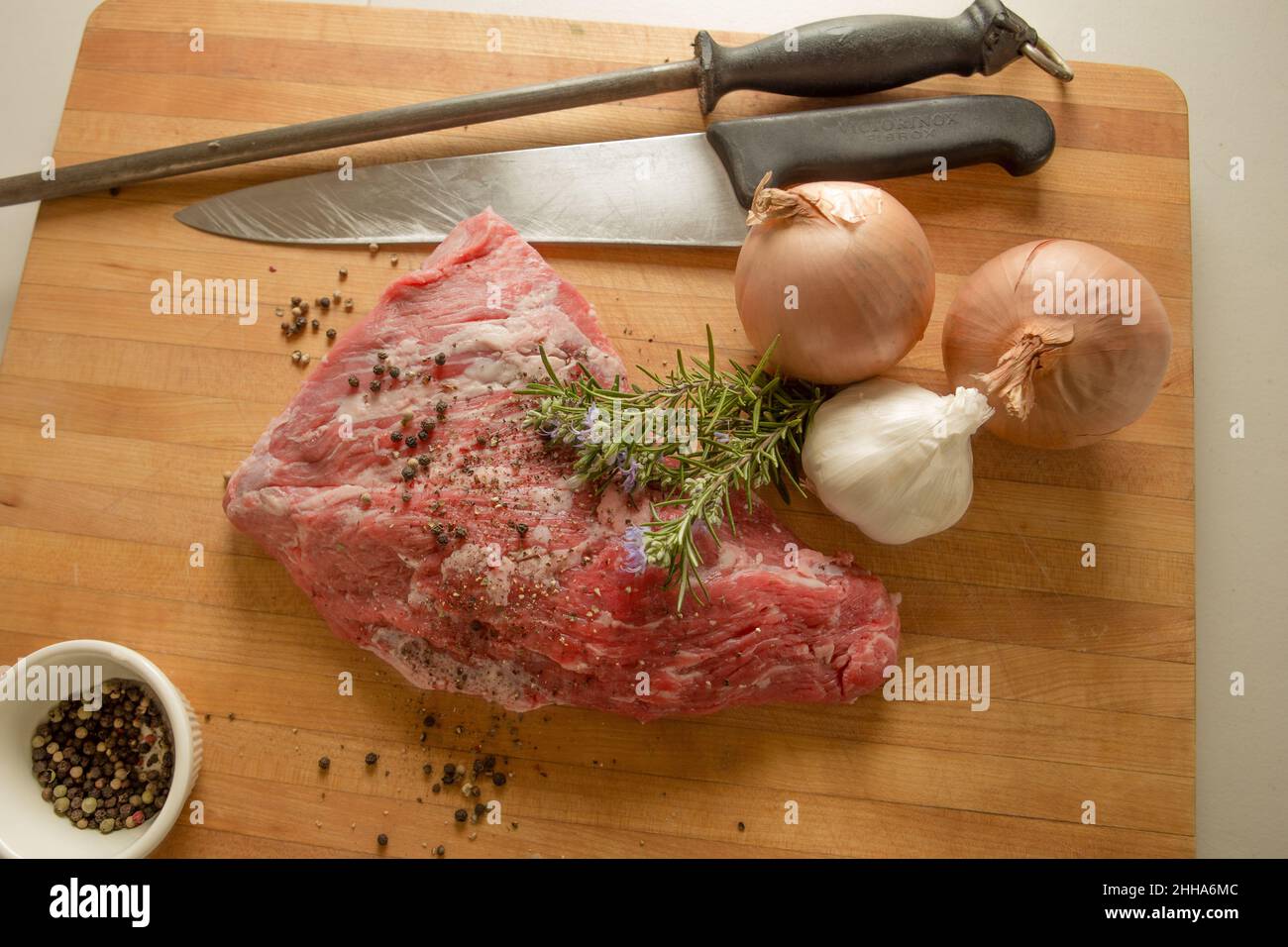 Versuchen Sie die Spitze des Rindfleischs auf einem Schneidebrett mit frischem Rosmarin, Salbei, Zwiebeln, Knoblauch, Pfeffer und Gewürzen. Köche Messer und Stahl schärfen. Stockfoto