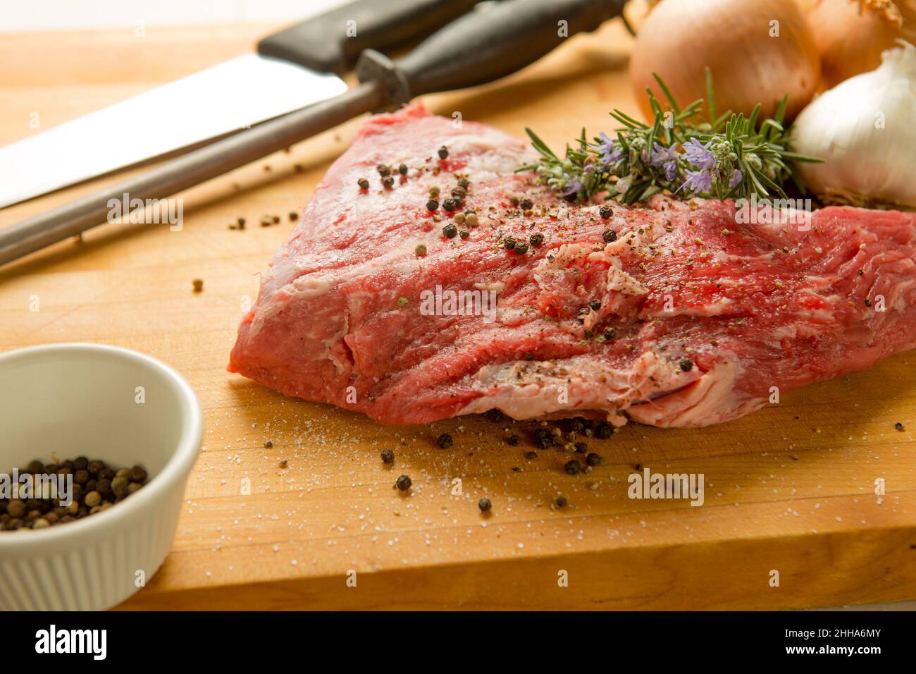 Versuchen Sie die Spitze des Rindfleischs auf einem Schneidebrett mit frischem Rosmarin, Salbei, Zwiebeln, Knoblauch, Pfeffer und Gewürzen. Köche Messer und Stahl schärfen. Stockfoto