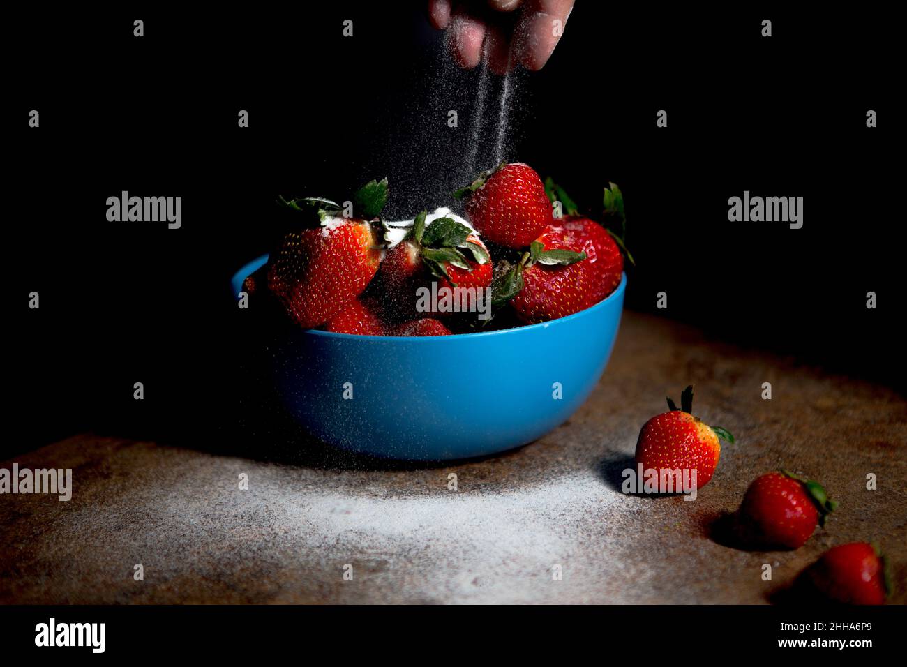 Eine blaue Schale mit frischen Erdbeeren mit einer Prise feinen Puderzuckers und dunkler und stimmungsvoller Beleuchtung Stockfoto