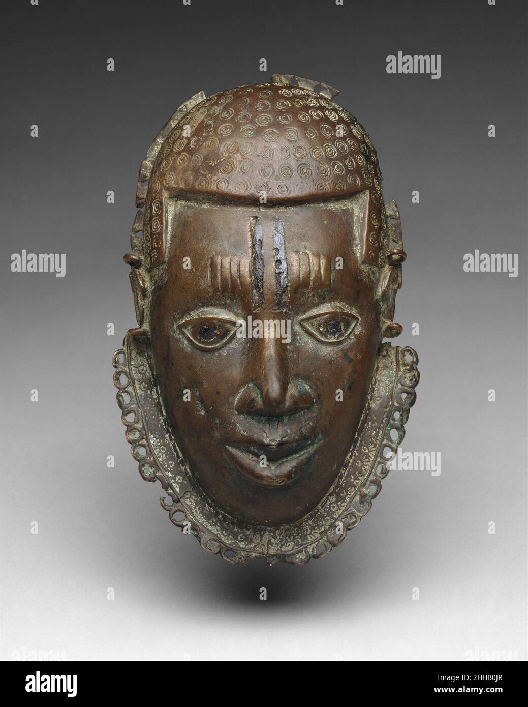 Pektoral: Gesicht 15th.–17th. Jahrhundert Edo-Völker warfen Messingmasken wie diese, die im Besitz von überragenden Häuptern und Titelverteidern des Benin-Königreichs waren. Diese Masken, die das Gesicht des oba selbst repräsentieren, wurden am Hals getragen, um den Rang anzuzeigen und dem König die Treue zu demonstrieren. Als Benin seinen politischen Einfluss und seine militärische Kontrolle über viele seiner Nachbarn ausweitete, erhielten auch die ausländischen Herrscher, die in sein politisches System aufgenommen wurden, diese Masken. Am Hof von königlichen Messingrollen geschaffen, wurden solche Werke von der oba an neu eingegliederte Häupter verteilt. Diese Arbeit ist es Stockfoto