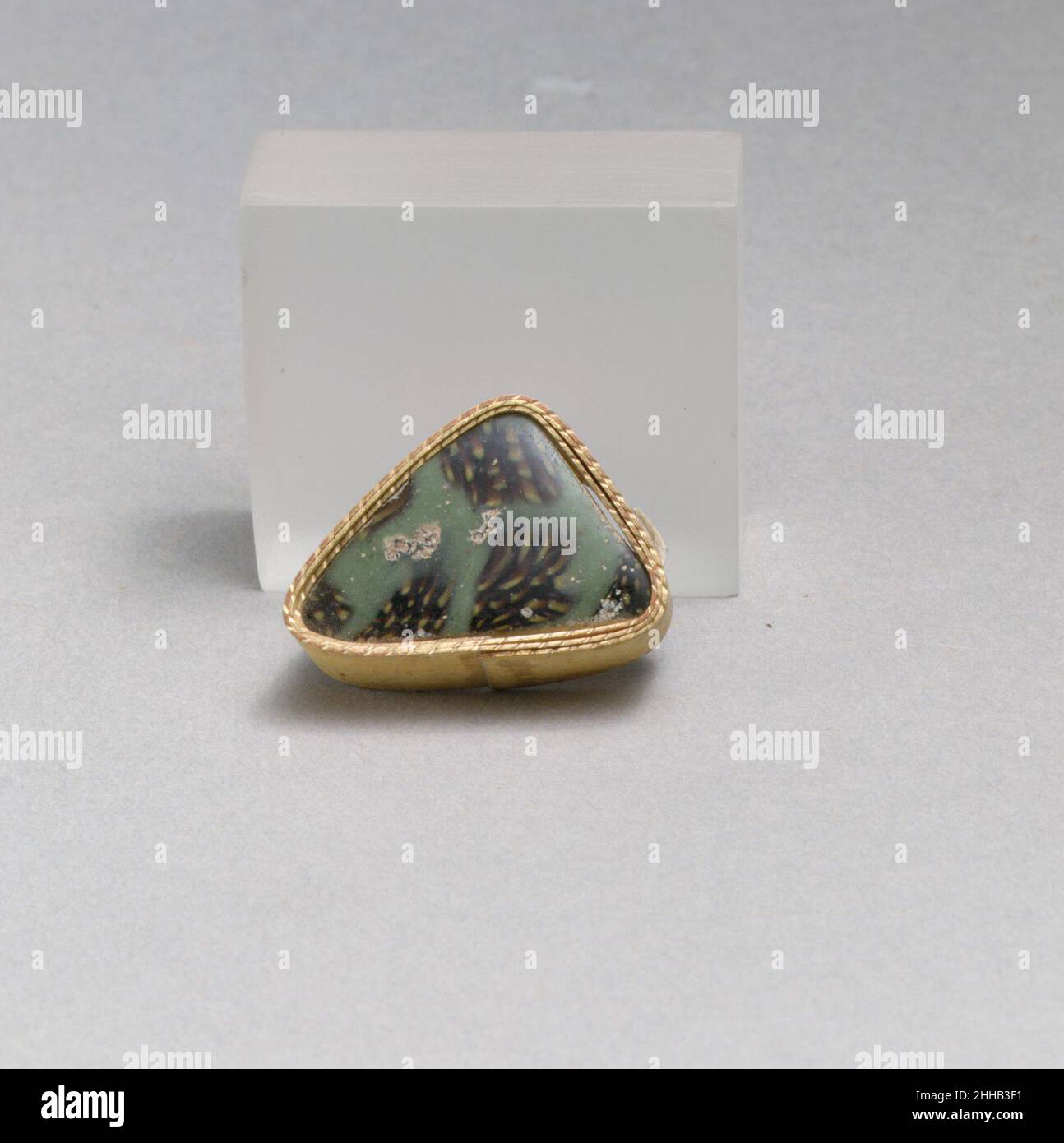 Glasmosaikfragment Ende des 1st. Jahrhunderts v. Chr.–Anfang des 1st. Jahrhunderts n. Chr. Römisches dünnwandiges Randfragment. Halbopakes graublaues, durchscheinendes tiefviolettes, schwarz erscheinendes und undurchsichtiges Gelb. Vertikaler, abgerundeter Rand; Flache gewölbte Seite, nach unten verjüngend.Mosaikmuster aus polygonalen Abschnitten eines einzelnen Rohres in einem violetten Boden gebildet, umrandet mit einem dicken, unregelmäßigen blauen Band und mit einer Streuung von gelben Punkten.Polierte Außenseite; Lochfraß und Verwitterung von Oberflächenblasen; Stumpfen, Lochfraß und schillernde Verwitterung auf dem Innenraum, am Rand und an den Kanten. In ein Dreieck schneiden. Glasmosaikfragment Stockfoto