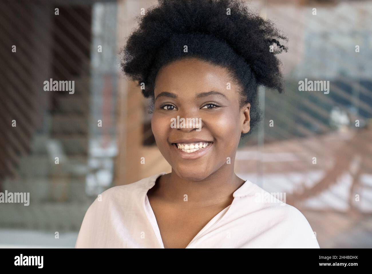 Die junge afroamerikanische Frau lächelt und schaut sich das Nahaufbildnis der Kamera an Stockfoto