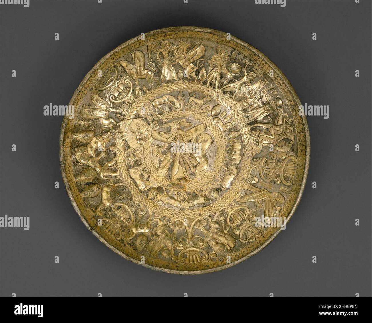 Silbervergoldete Schale ca. 725–675 v. Chr. Zypern der zentrale Tondo zeigt eine geflügelte Gottheit assyrischen Typs, die einen grassierenden Löwen mit einem Schwert fällte. Der umgebende Fries zeigt eine Vielzahl von Tier- und Erzählmotiven, darunter zwei spezifisch ägyptische Motive: Eine Sphinx mit der ägyptischen Doppelkrone und ein Löwe, der über einen toten Mann trete und damit den pharao symbolisiert, der seine Feinde dominiert. Das breite Außenband bietet eine Vielzahl von Kämpfen. Von größter Bedeutung sind jedoch zwei Inschriften. Oben, über einer assyrischen Figur, die einen Löwen tötete, steht eine zypriotische Silbenschrift mit der Aufschrift: „Ich bin [der Bogen Stockfoto