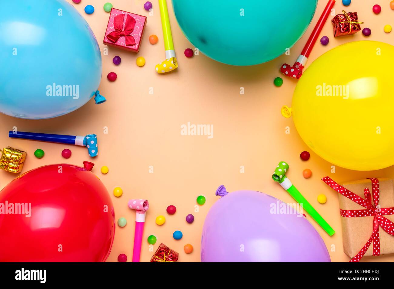 Farbenfroher Partyrahmen mit roter Geschenkbox mit verschiedenen Party-Konfetti, Luftballons, Luftschlangen, Pokern und Dekorationen auf beigem Hintergrund. Urlaubskarte flach Stockfoto