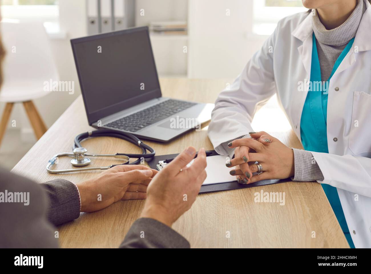 Unbekannter Arzt und Patient sprechen während der ärztlichen Konsultation, während er am Tisch im Büro sitzt. Stockfoto