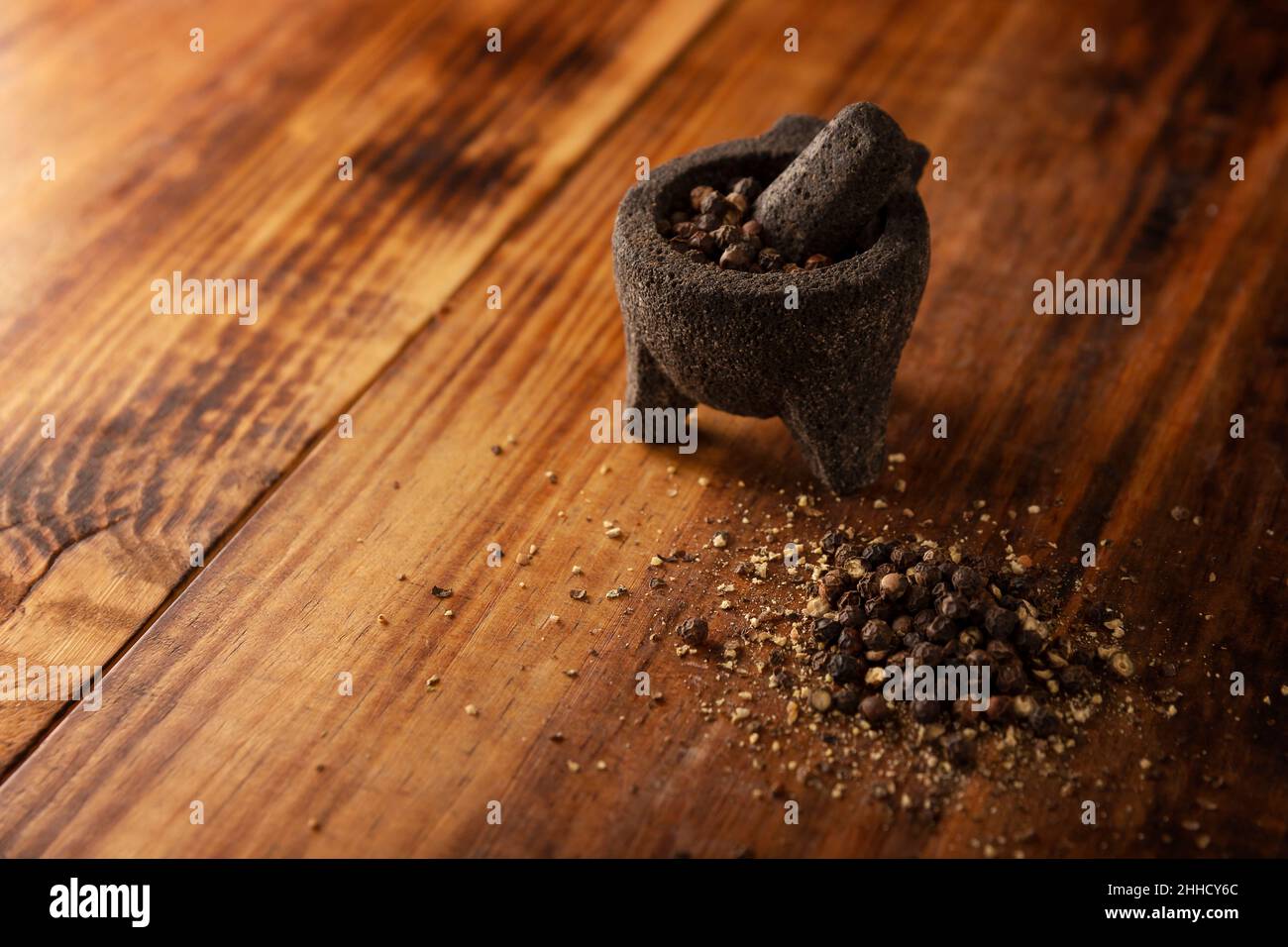 Schwarze Pfefferkörner in einem kleinen Molcajete (traditionelle mexikanische Version von Mörtel und Stößel) auf rustikalem Holzhintergrund. Kopieren Sie Platz für Ihren Text Stockfoto