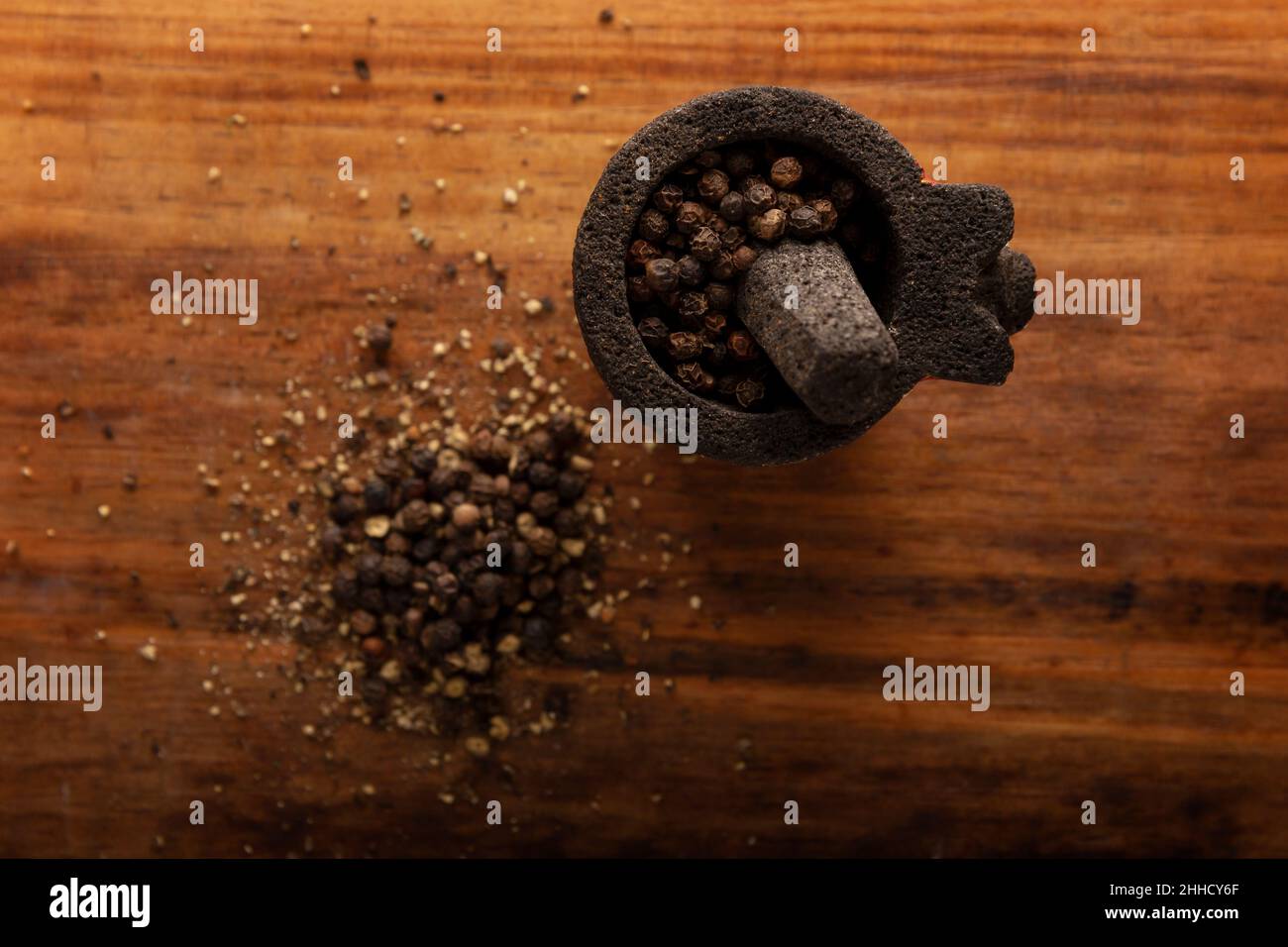 Schwarze Pfefferkörner in einem kleinen Molcajete (traditionelle mexikanische Version von Mörtel und Stößel) auf rustikalem Holzhintergrund. Flach lay-Bild. Nahaufnahme Stockfoto