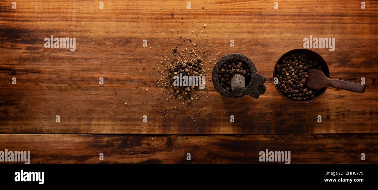 Schwarze Pfefferkörner in einem kleinen Molcajete (traditionelle mexikanische Version von Mörtel und Stößel) und kleine Schüssel auf rustikalem Holzhintergrund. Stockfoto