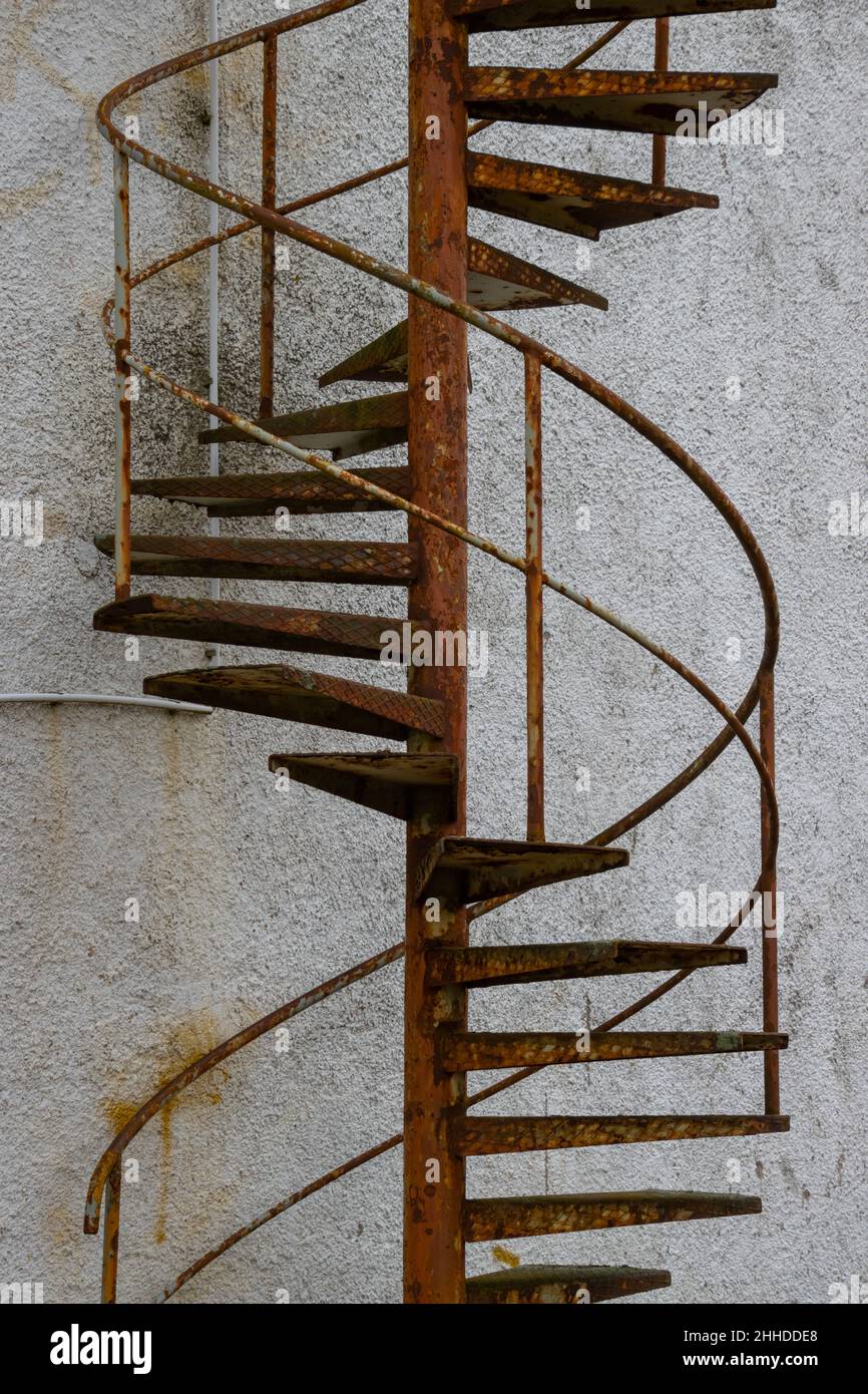 Alte rostige Wendeltreppe, die zu einer geschlossenen Tür vor einem alten Gebäude führt Stockfoto