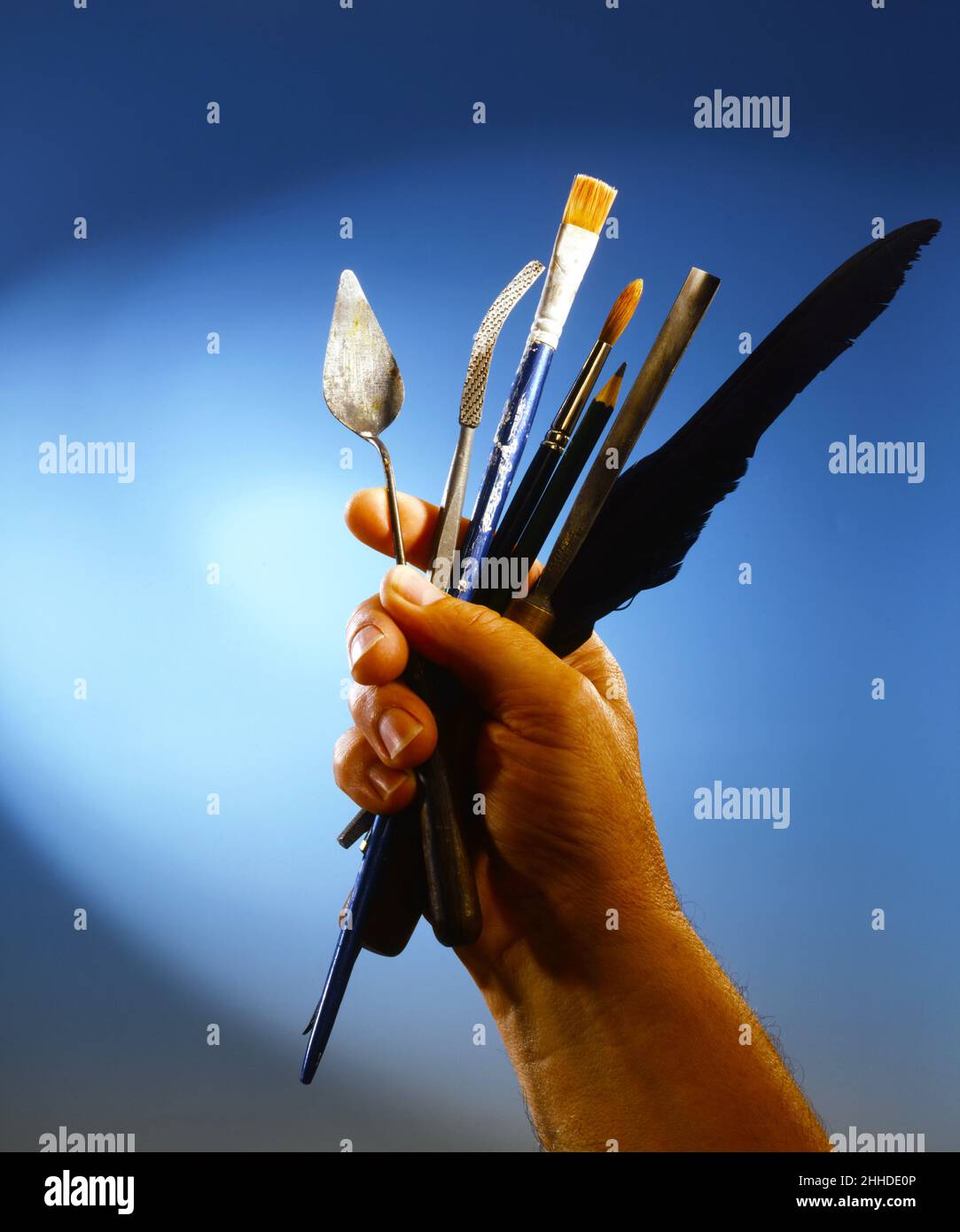 Männliche Hand hält Künstler Werkzeuge auf einem dunkelblauen Hintergrund kopieren Space Pinsel Malen Messer Federn Schaber Palette Messer Stockfoto