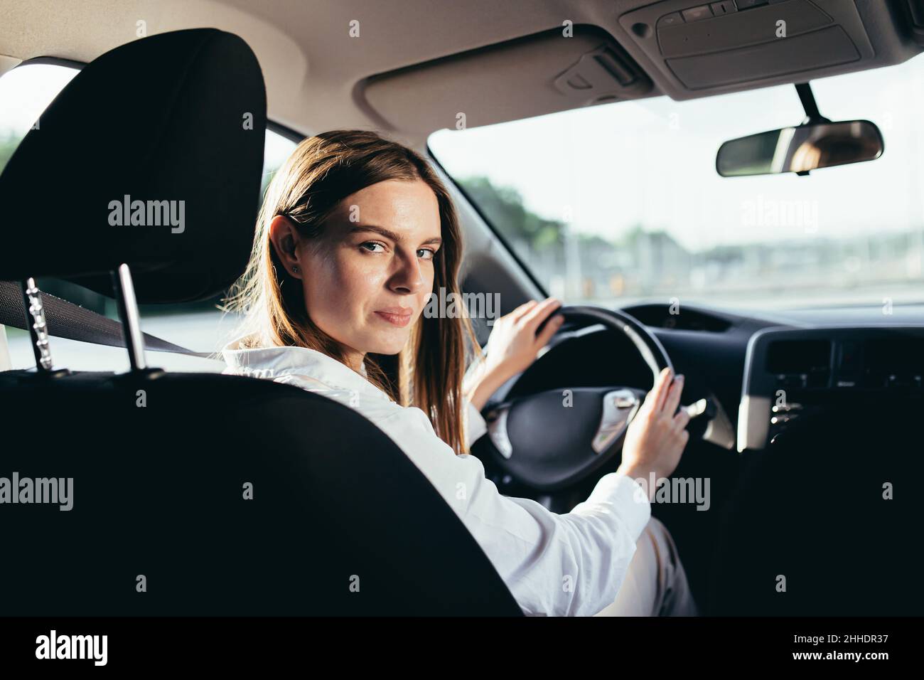 Porträt einer erfolgreichen Frau, die ein Auto fährt, fröhlich lächelt und die Kamera anschaut Stockfoto