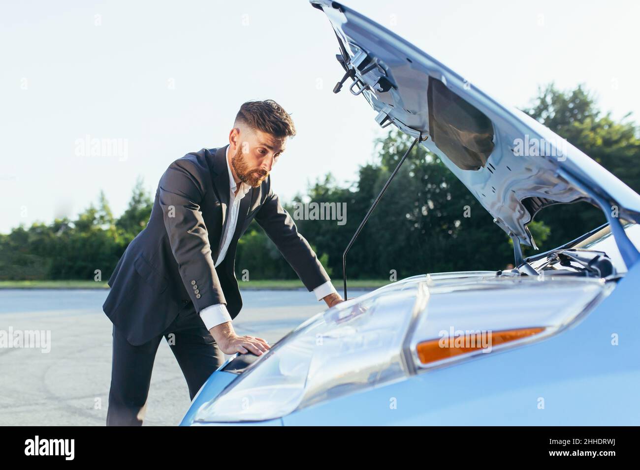 Verwirrt Mann in einem Business-Anzug untersucht den Motor des Autos Stockfoto