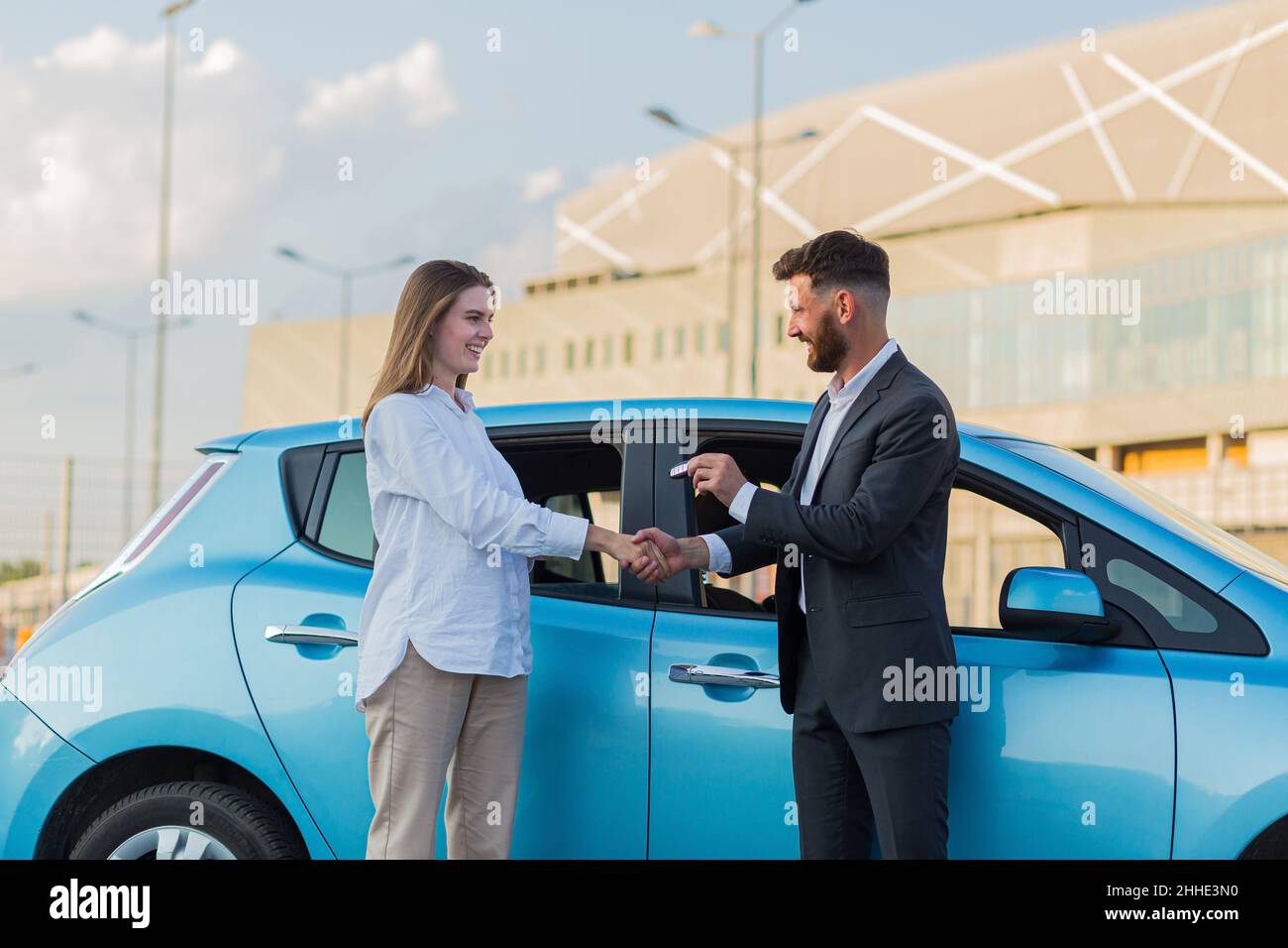 Der männliche Autoverkäufer übergibt die Schlüssel an die Käuferin, der Kaufvertrag ist erfolgreich abgeschlossen Stockfoto