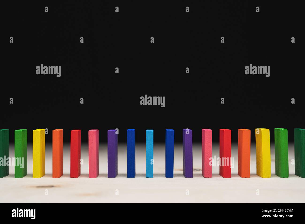 Farbige Dominosteine in einer Reihe von Regenbogenfarben aufgereiht. Heller Vordergrund und schwarzer Hintergrund mit Kopierbereich. Stockfoto