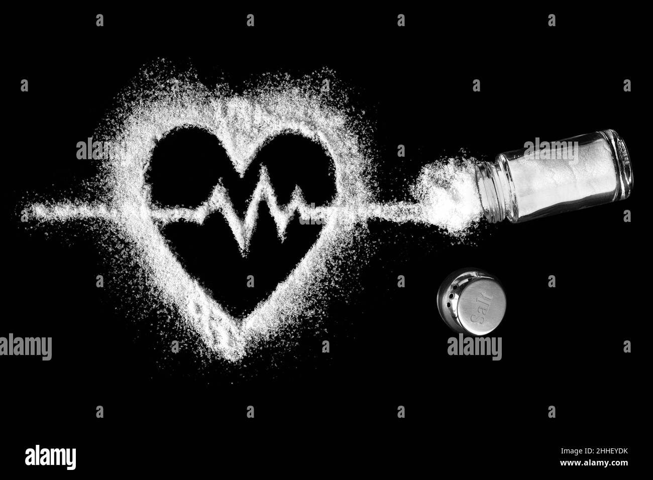 Herzförmiges Salz mit einem Kardiogramm im Inneren mit einem Salzstreuer mit bestreutem Salz. Konzept für kardiovaskuläre Probleme. Der Schaden einer erhöhten Salzaufnahme. Stockfoto