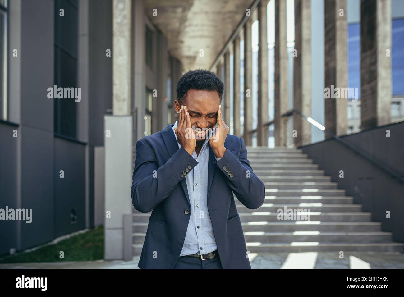 Erschöpfter junger afroamerikanischer Geschäftsmann Büroangestellter steht im Freien. Gestresster überarbeiteter schwarzer Mann mit Kopfschmerzen massiert den Kopf. Ti.-Druck Stockfoto