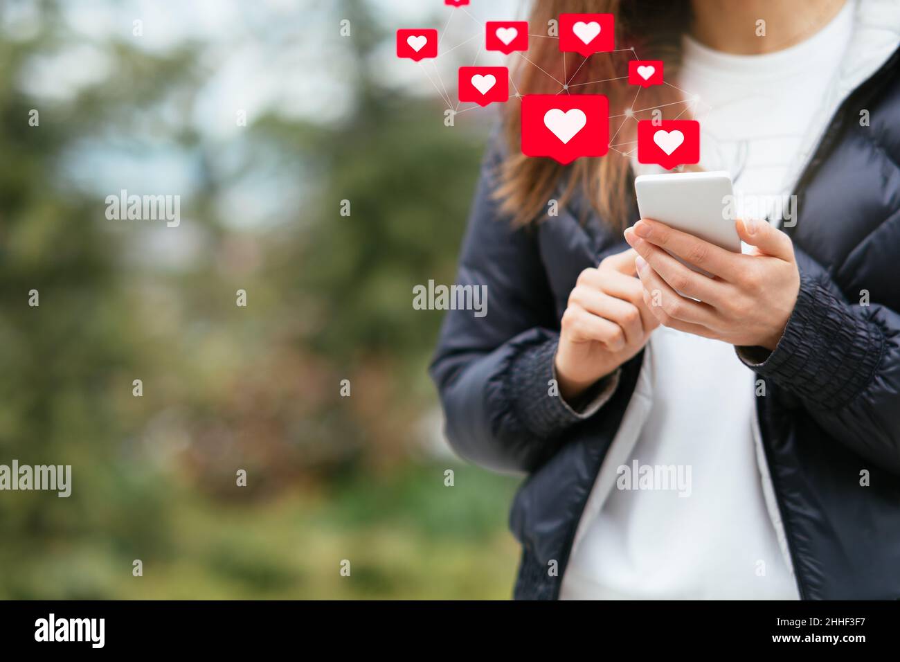 Interaktionen in sozialen Medien auf dem Mobiltelefon. Junge Frau hält das Smartphone mit „Gefällt mir“- und „Liebe“-Symbolen, während sie im Freien steht Stockfoto