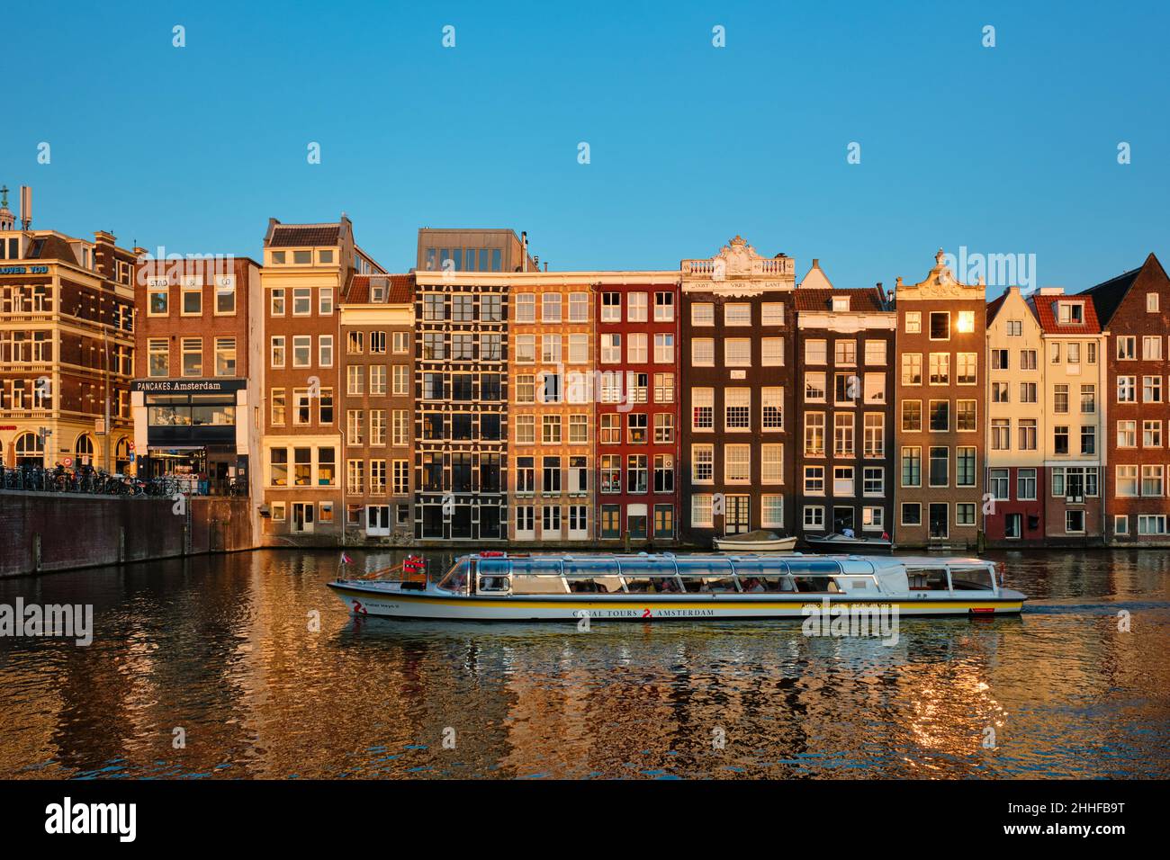 Grachtenrundfahrt mit Touristenboot in Amsterdam am Damrak-Kanal und Pier. Stockfoto