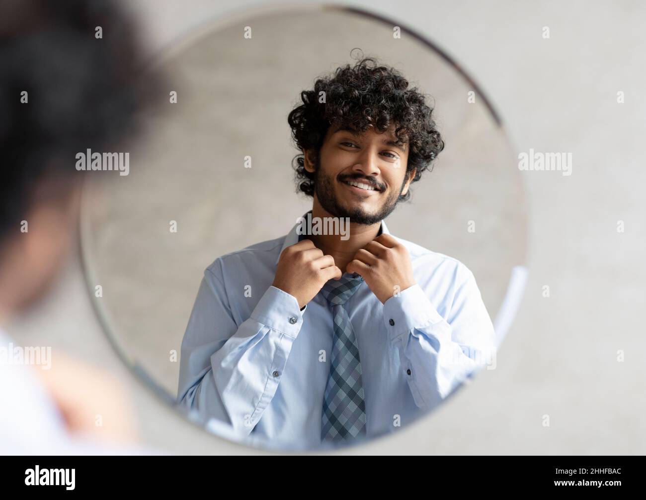 Aufgeregter indischer Geschäftsmann, der sich fertig macht und Hemd aufknöpft, im Badezimmer vor dem Spiegel stehend Stockfoto