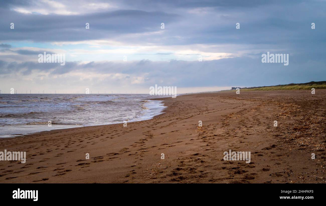 Weite Aufnahme von Tierspuren im Sand am Strand von Anderby Creek, Lincolnshire mit Blick auf das Dorf und ein paar nicht erkennbare Menschen Stockfoto