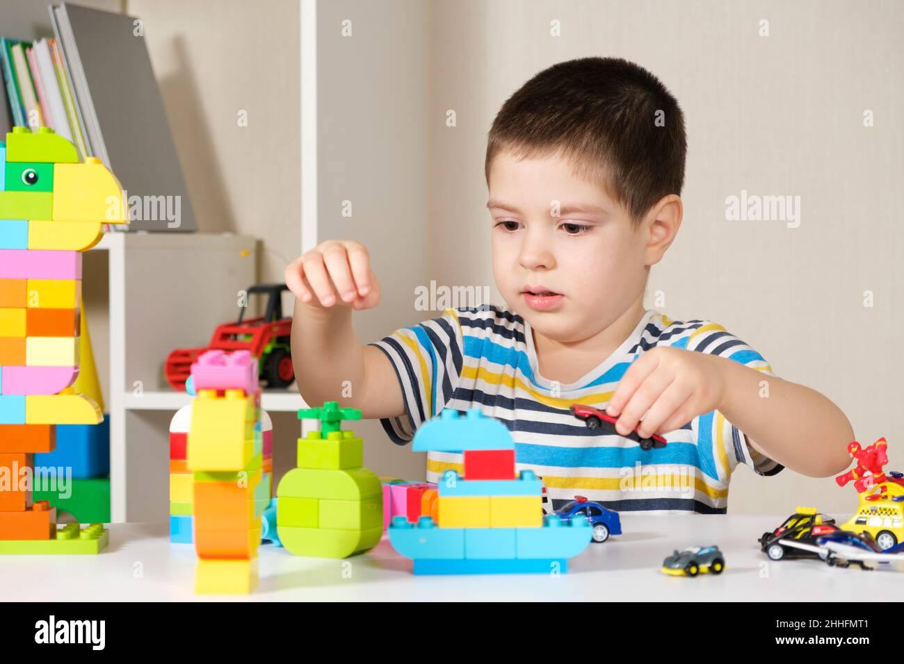 Ein hübscher Junge von 4 Jahren spielt mit den Autos und dem Bausatz, den Spielen der Vorschulkinder, der Entwicklung der Phantasie. Stockfoto