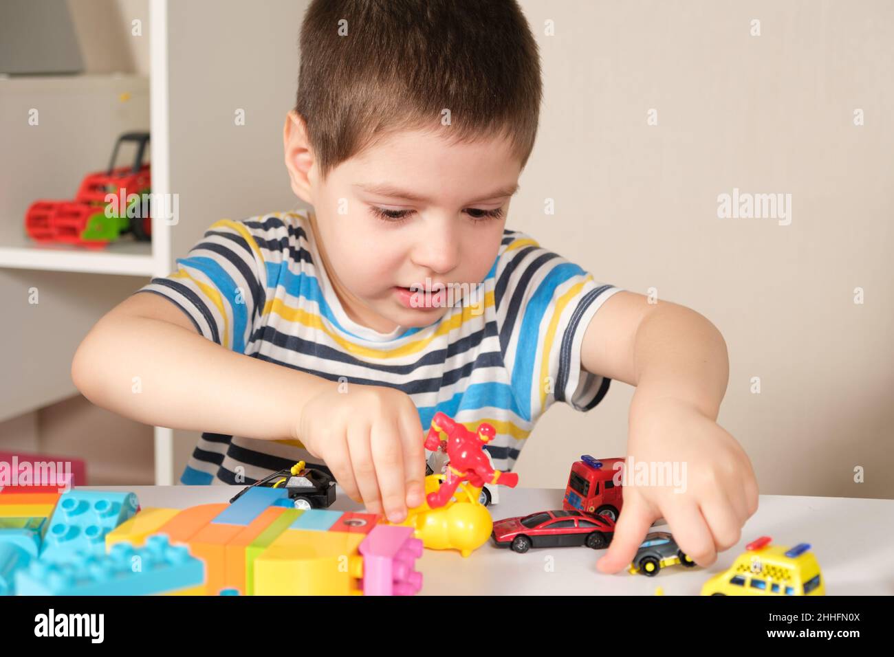 Ein hübscher Junge von 4 Jahren spielt mit den Autos und dem Bausatz, den Spielen der Vorschulkinder, der Entwicklung der Phantasie. Stockfoto