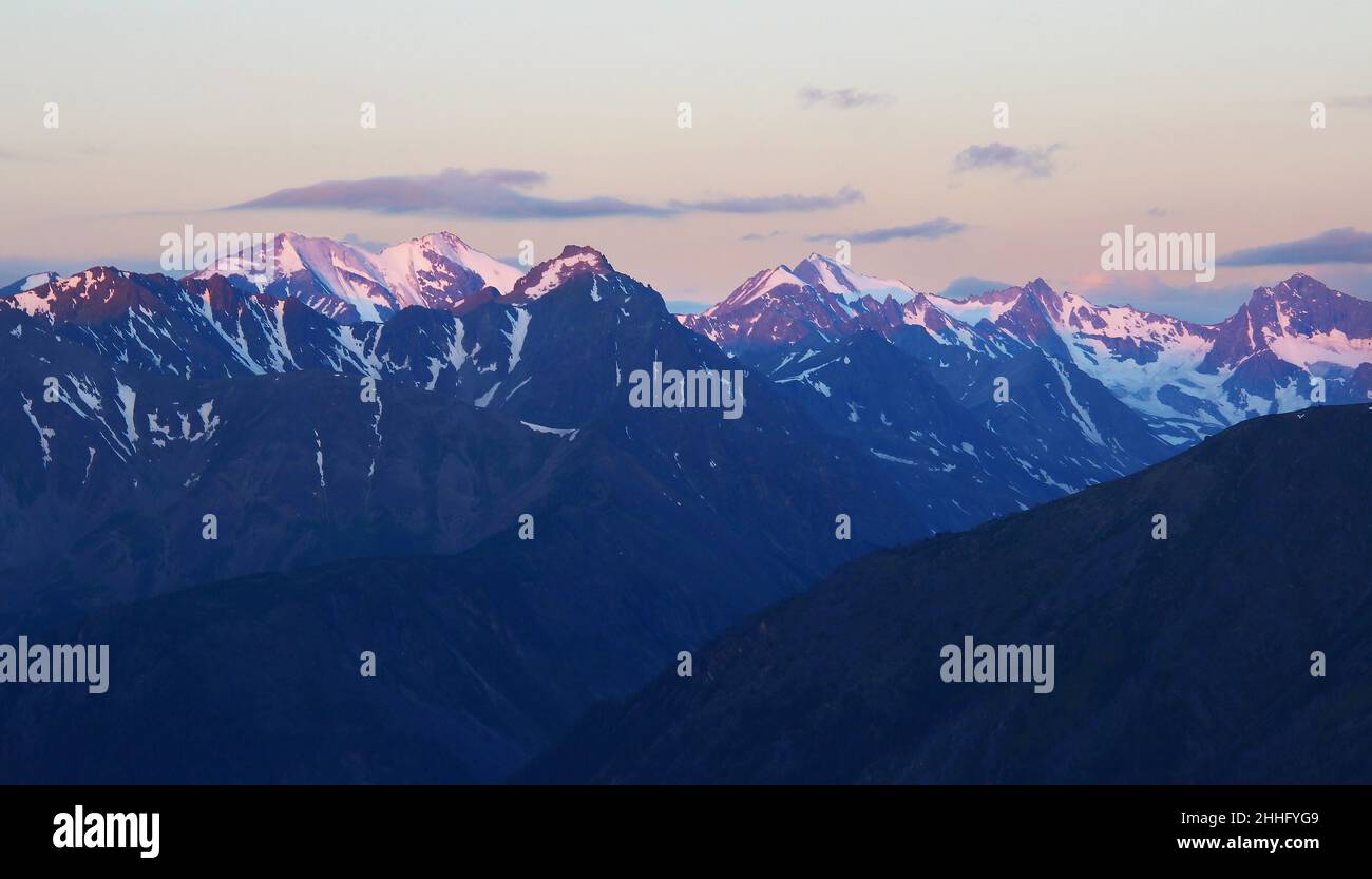 Langer Bergrücken mit schneebedeckten Gipfeln bei Sonnenaufgang in rosa Licht im Altai Stockfoto