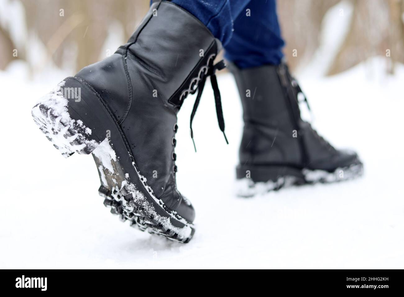 Weibliche Beine in schwarzen Leder Schnürstiefeln auf Schnee. Frau, die auf der Winterstraße läuft, warme Schuhe für kaltes Wetter Stockfoto