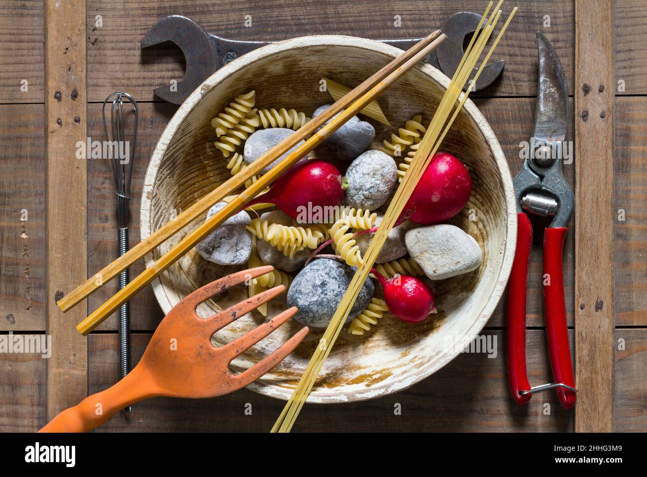 Teller mit Steinen, rotem Rettich, Gabel und Werkzeug, Schraubenschlüssel und Zange als Besteck auf einem Brett angeordnet - symbolisches Stillleben Bild von Hoffnung, Hunger und Armut Stockfoto