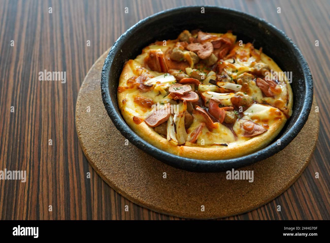 Barbeque-Pizza-Hütte mit Rind, serviert auf einem schwarzen Teller oder einer Schüssel mit einem braunen strukturierten Holztisch im Hintergrund. Gewürzte Bratkartoffeln auf einem weißen Teller serviert. Stockfoto